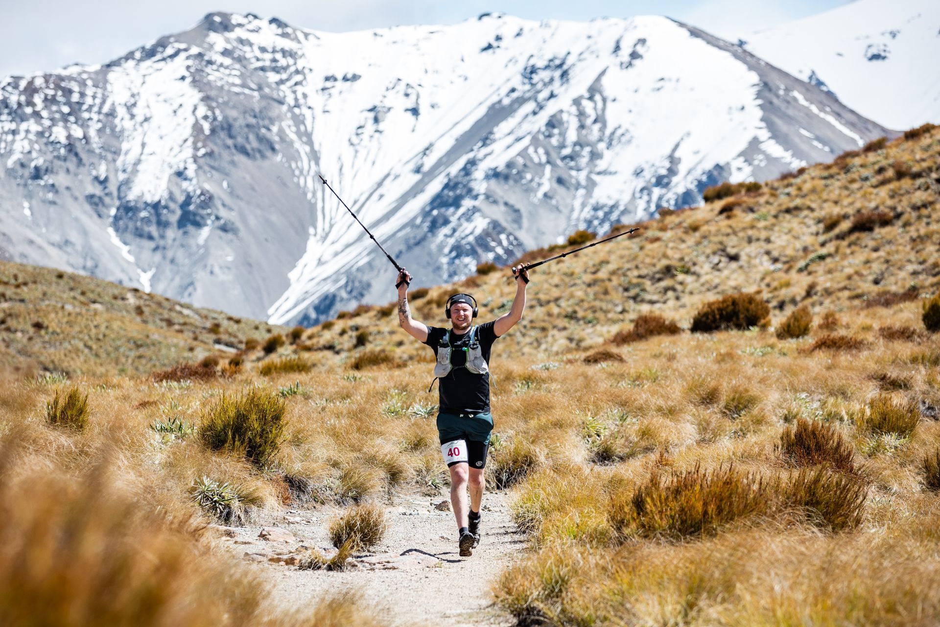 A man is running on a trail in the mountains with a mountain in the background.