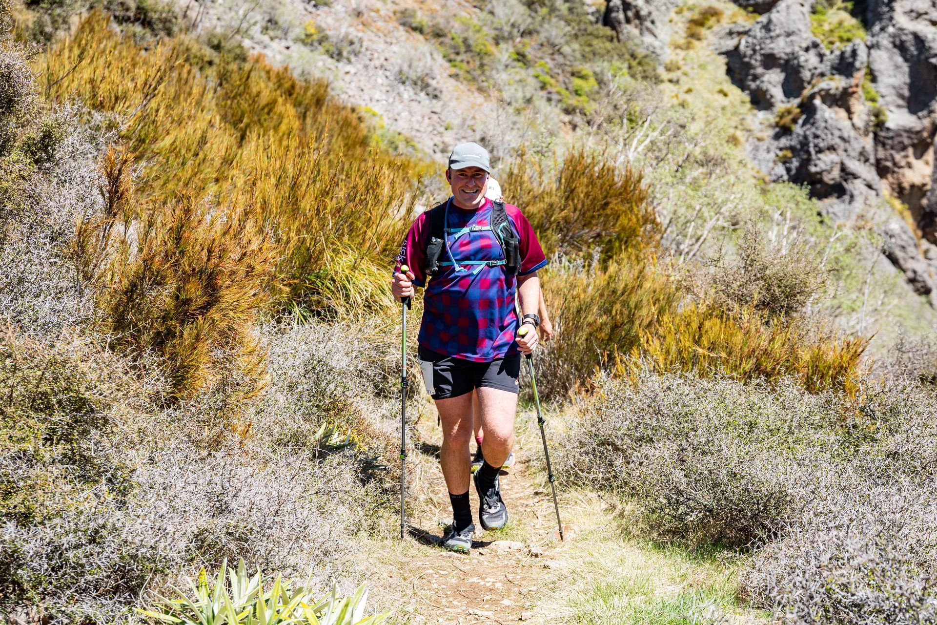 A man is walking down a trail with hiking poles.