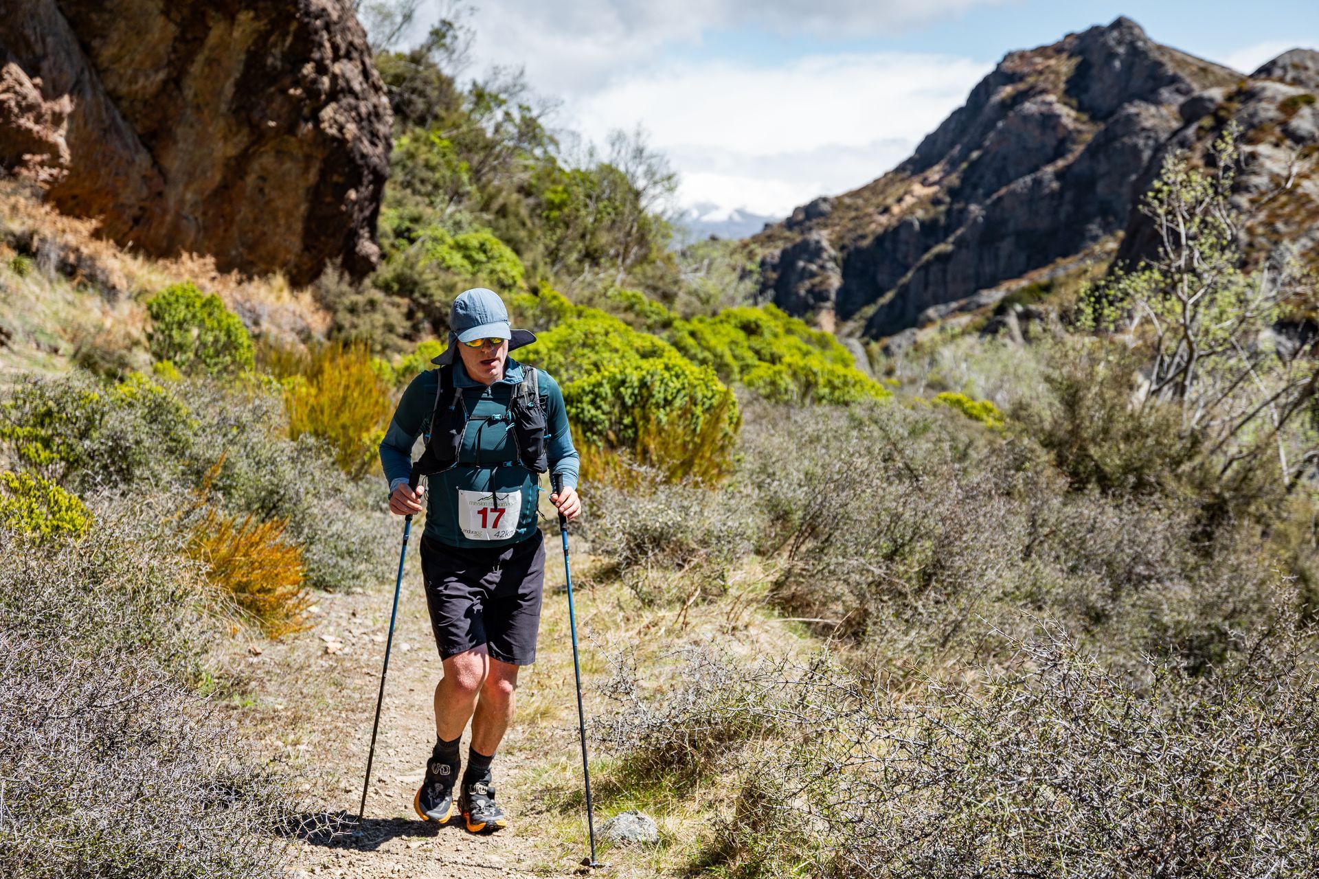 A man is walking on a trail in the mountains with hiking poles.