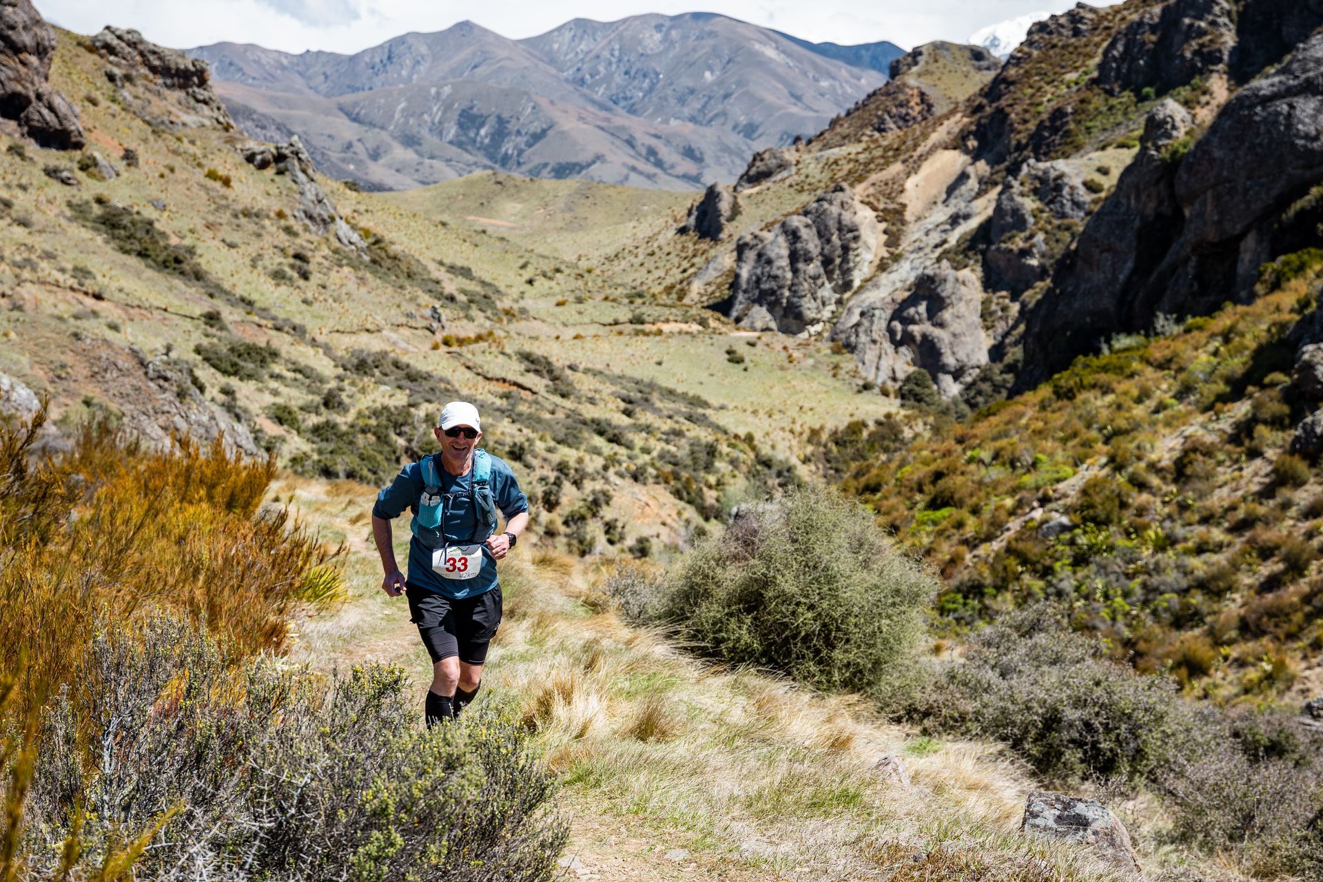 A man is running down a trail in the mountains.