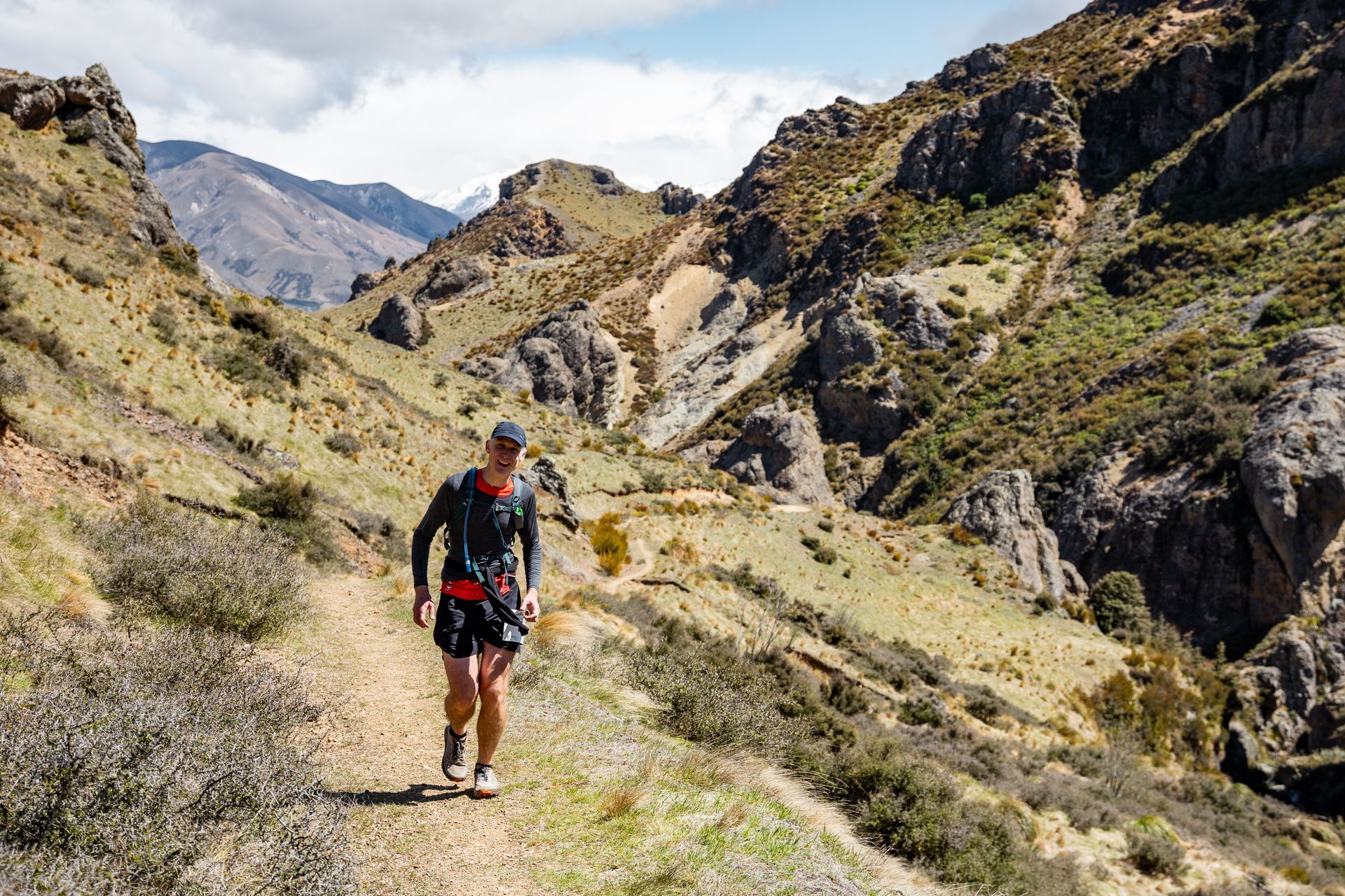 A man is walking down a dirt path in the mountains.