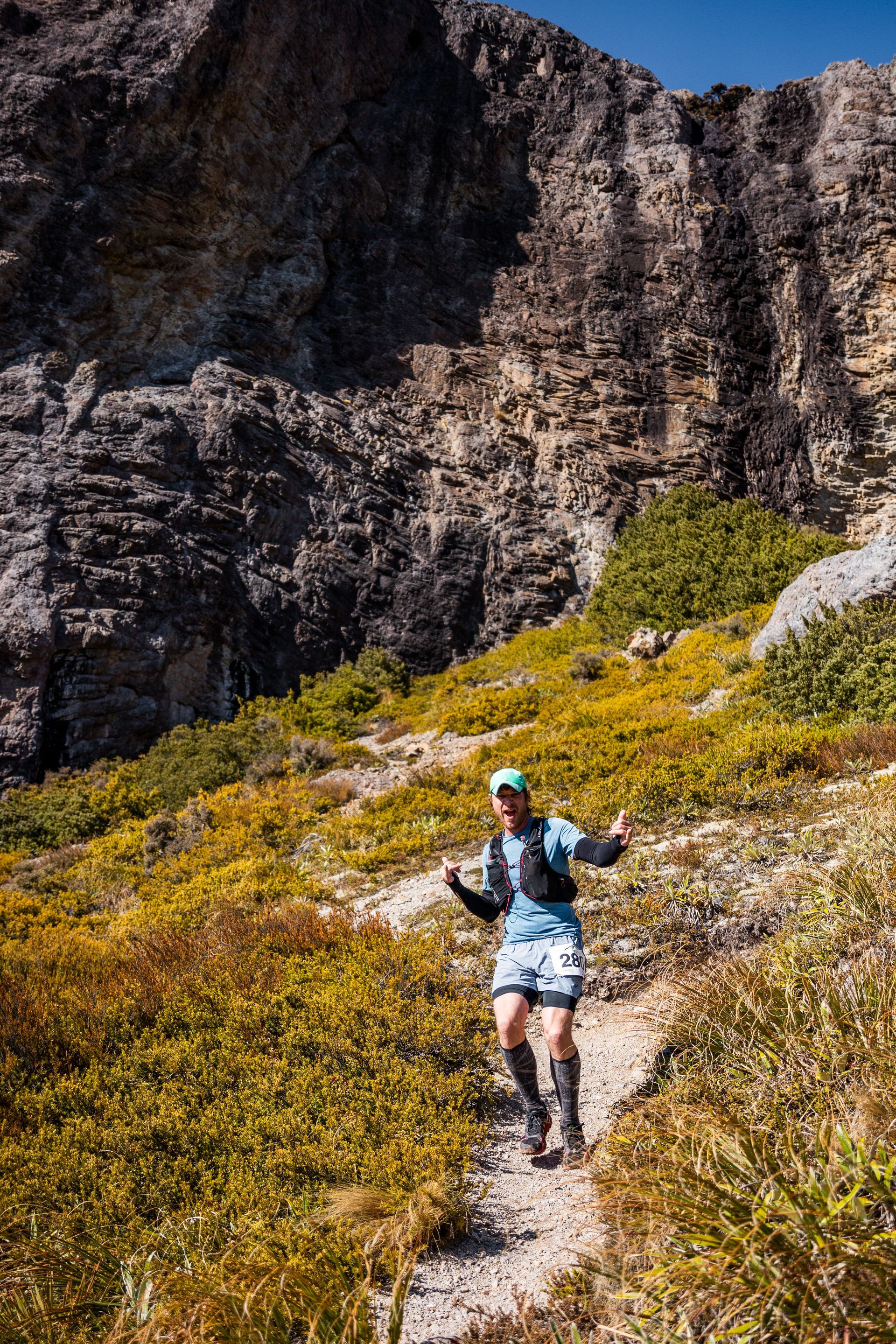 A man is running down a trail in the mountains.