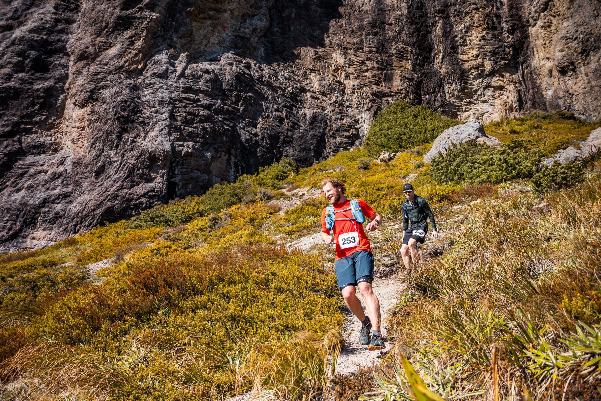 Two people are running up a hill on a trail.