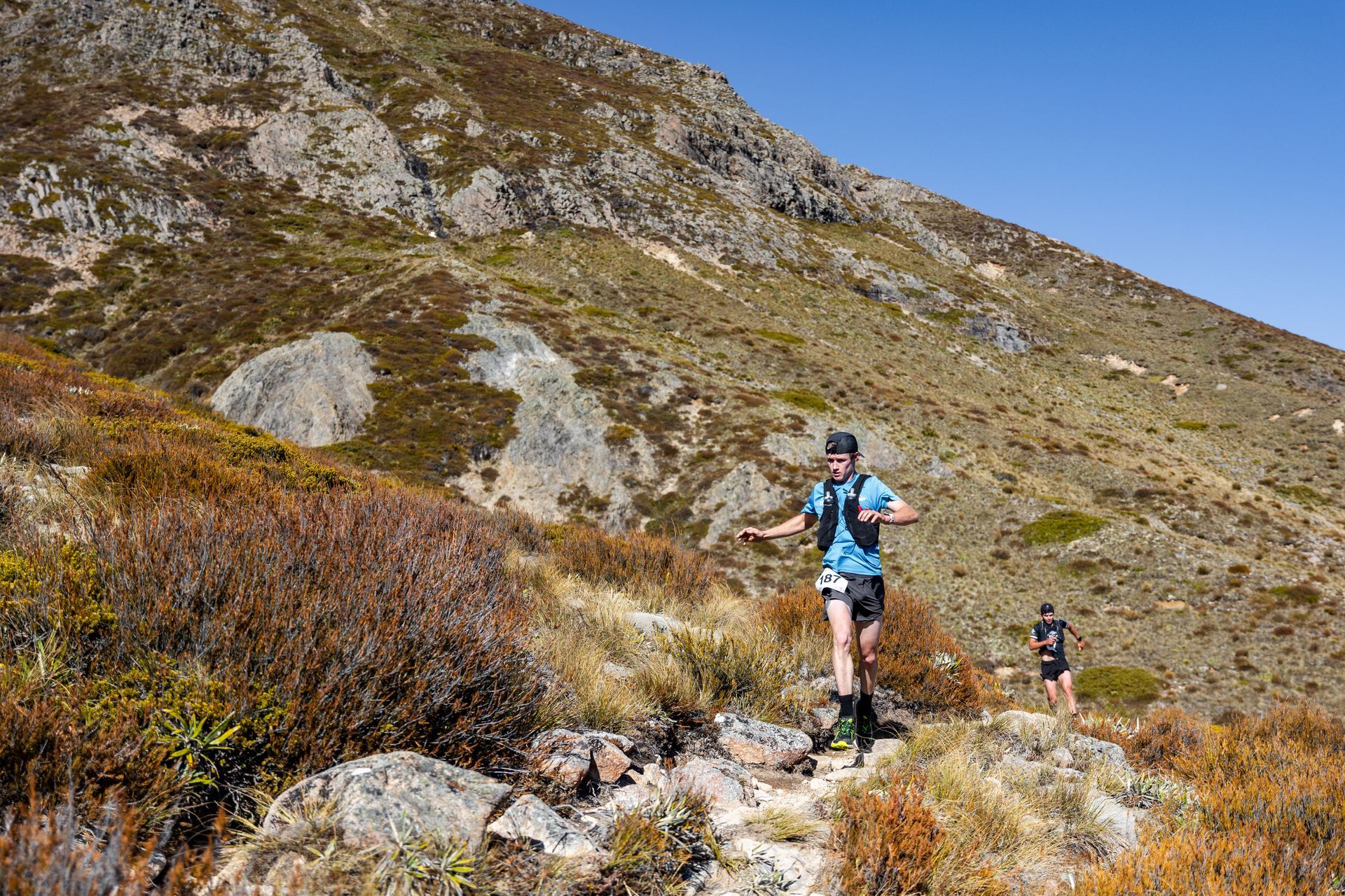 A man and a woman are running on a trail in the mountains.