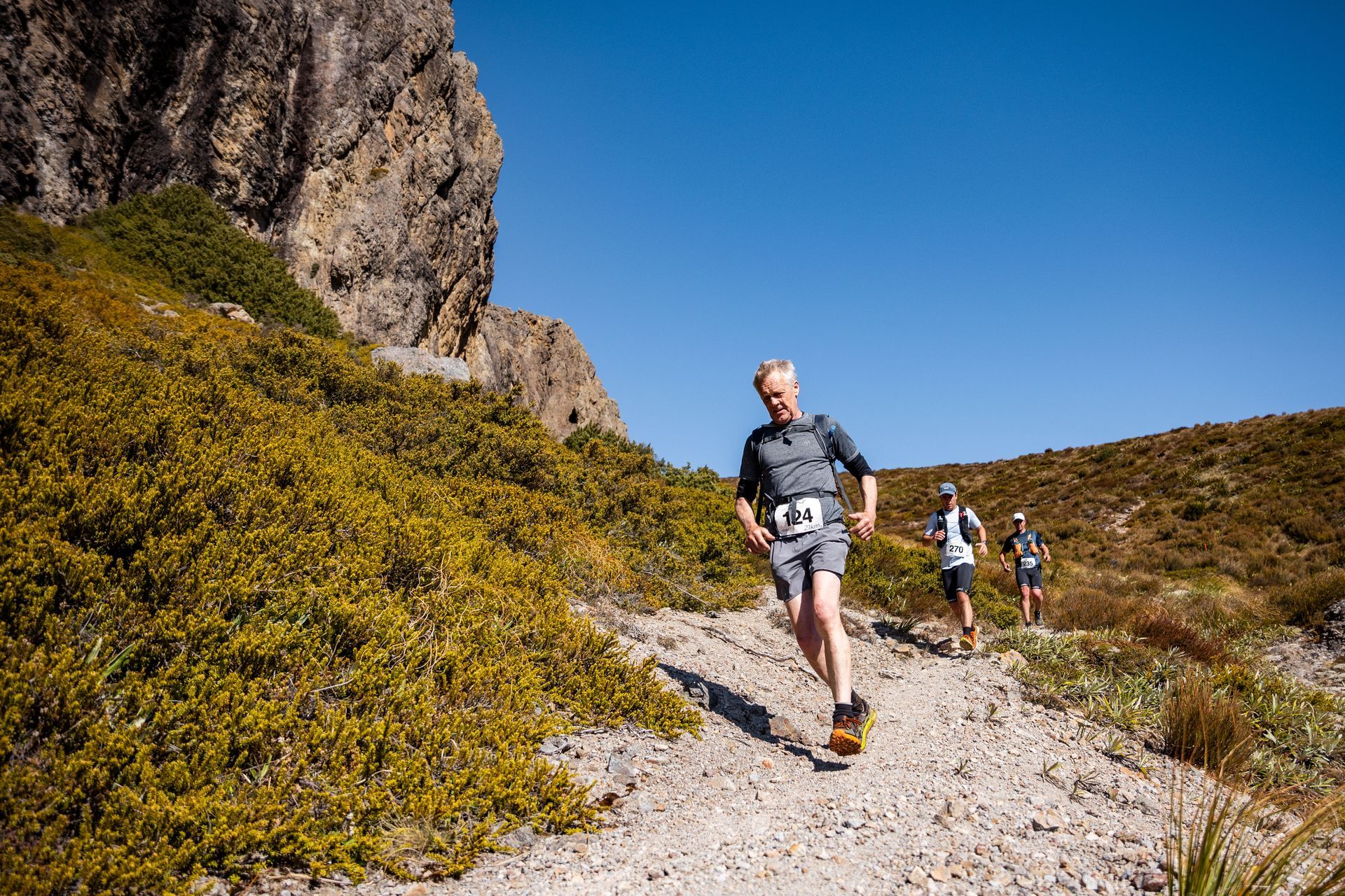 A group of people are running down a dirt path in the mountains.
