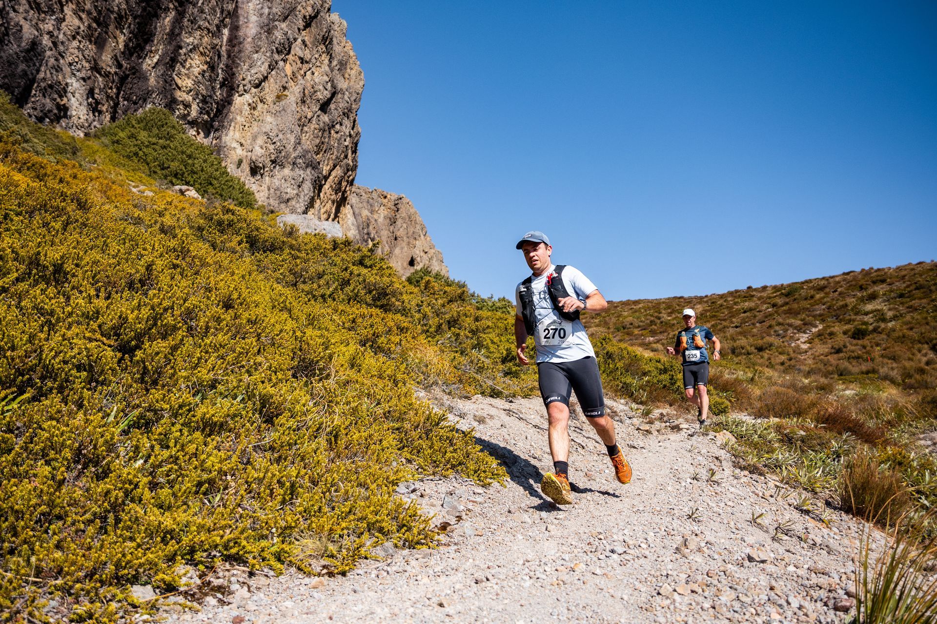 Two men are running on a dirt path in the mountains.