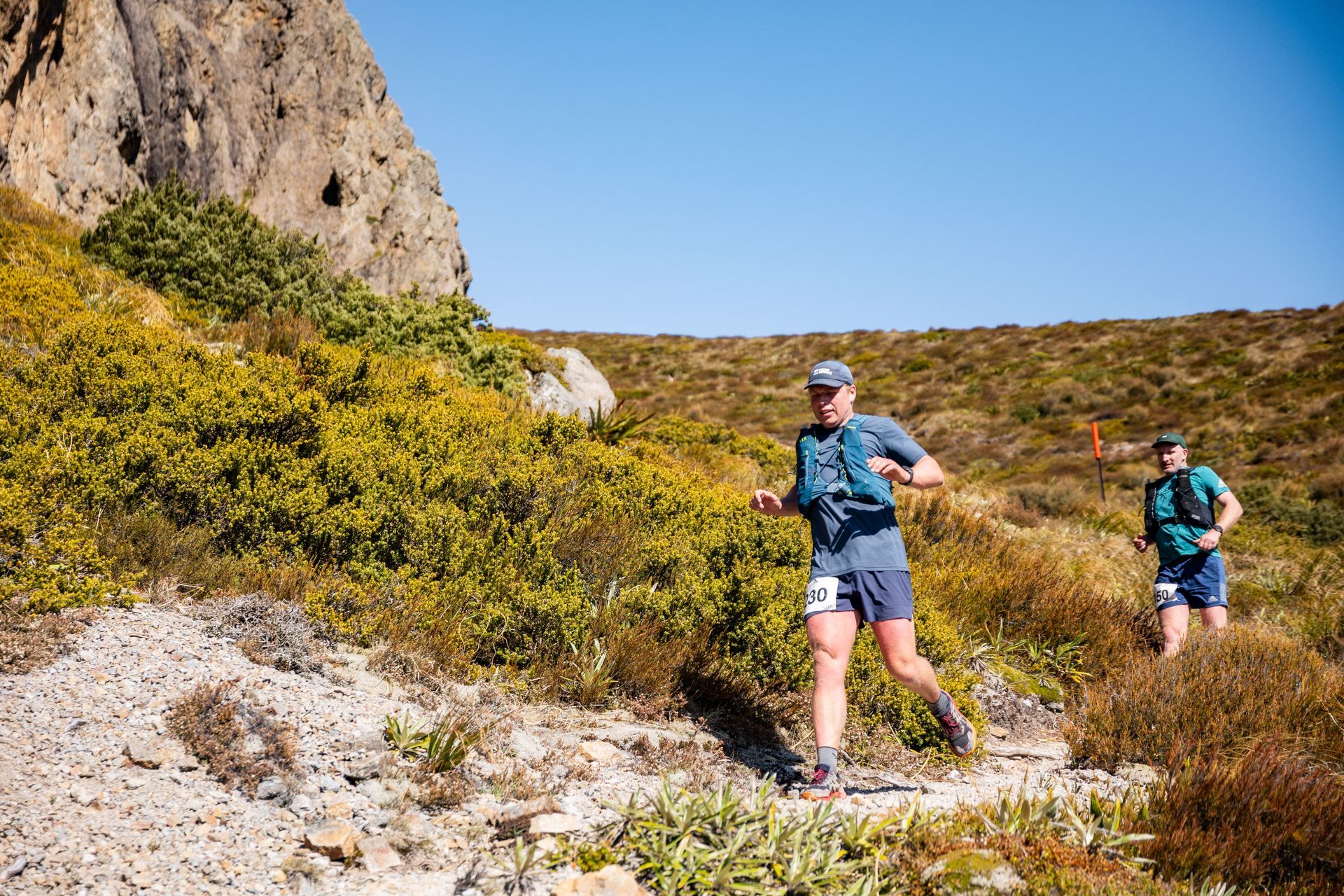 Two people are running on a trail in the mountains.