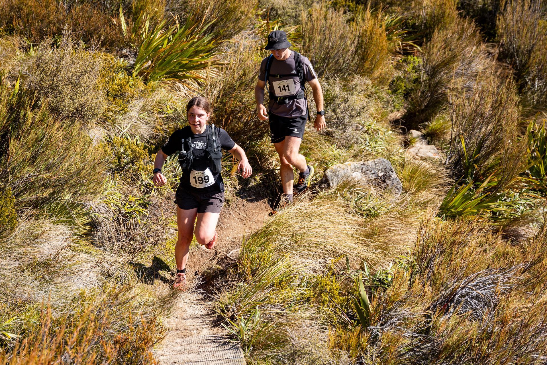 A man and a woman are running down a trail in the woods.