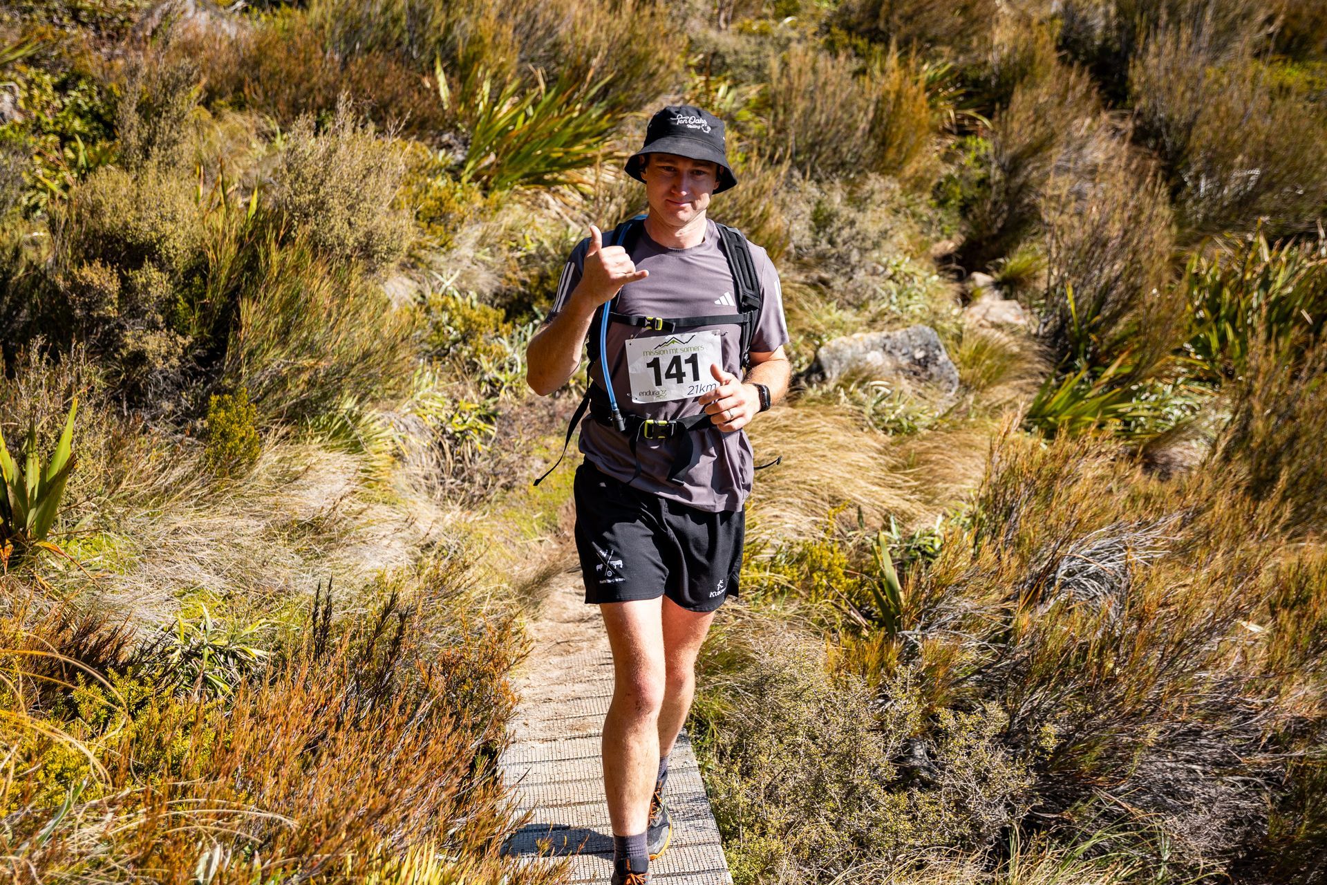A man is running on a trail in the woods and giving a thumbs up.