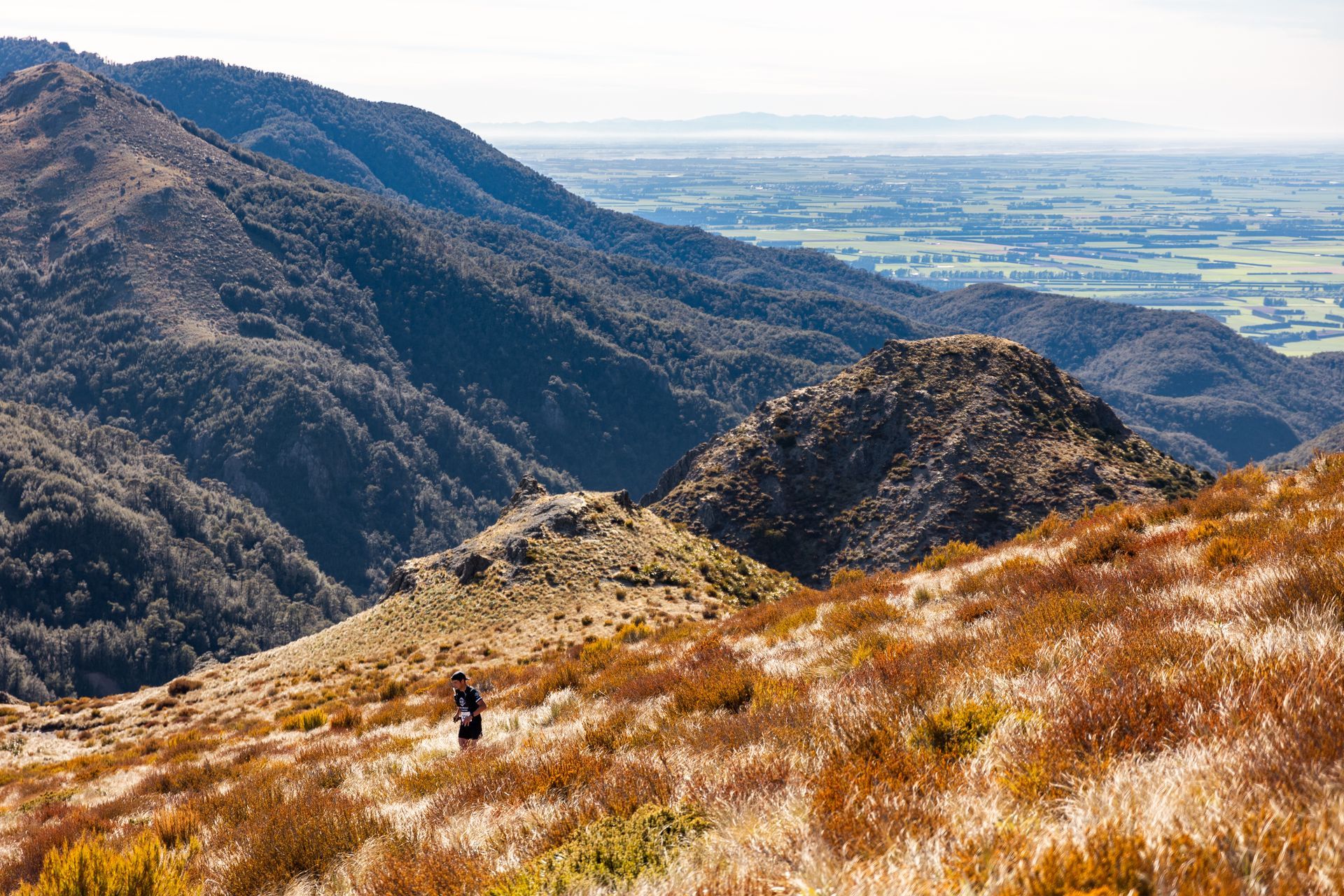 A person is standing on top of a hill with mountains in the background.