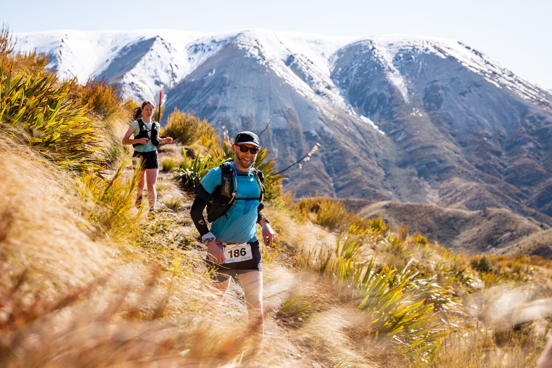 A man and a woman are running on a trail in the mountains.