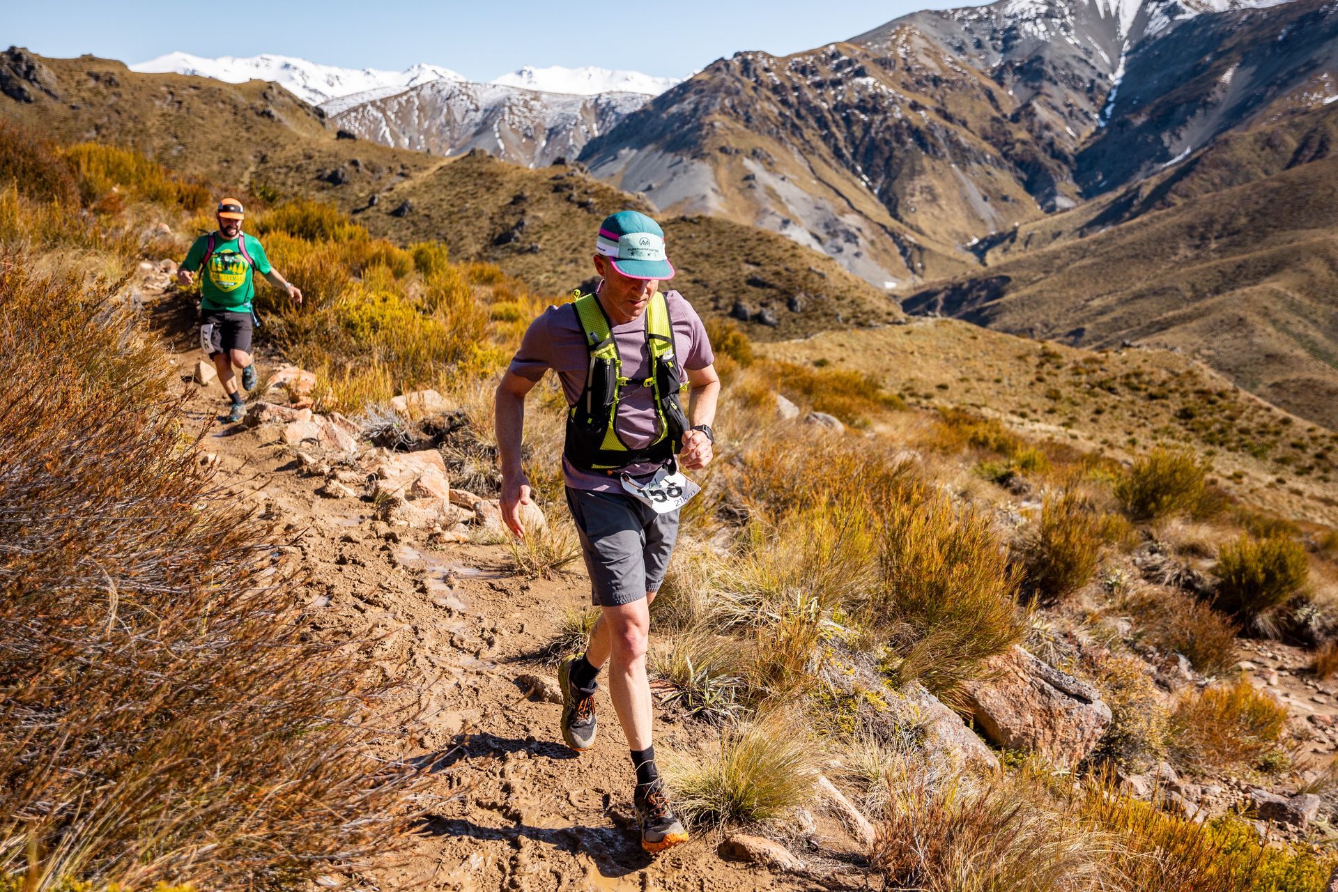 Two men are running on a trail in the mountains.