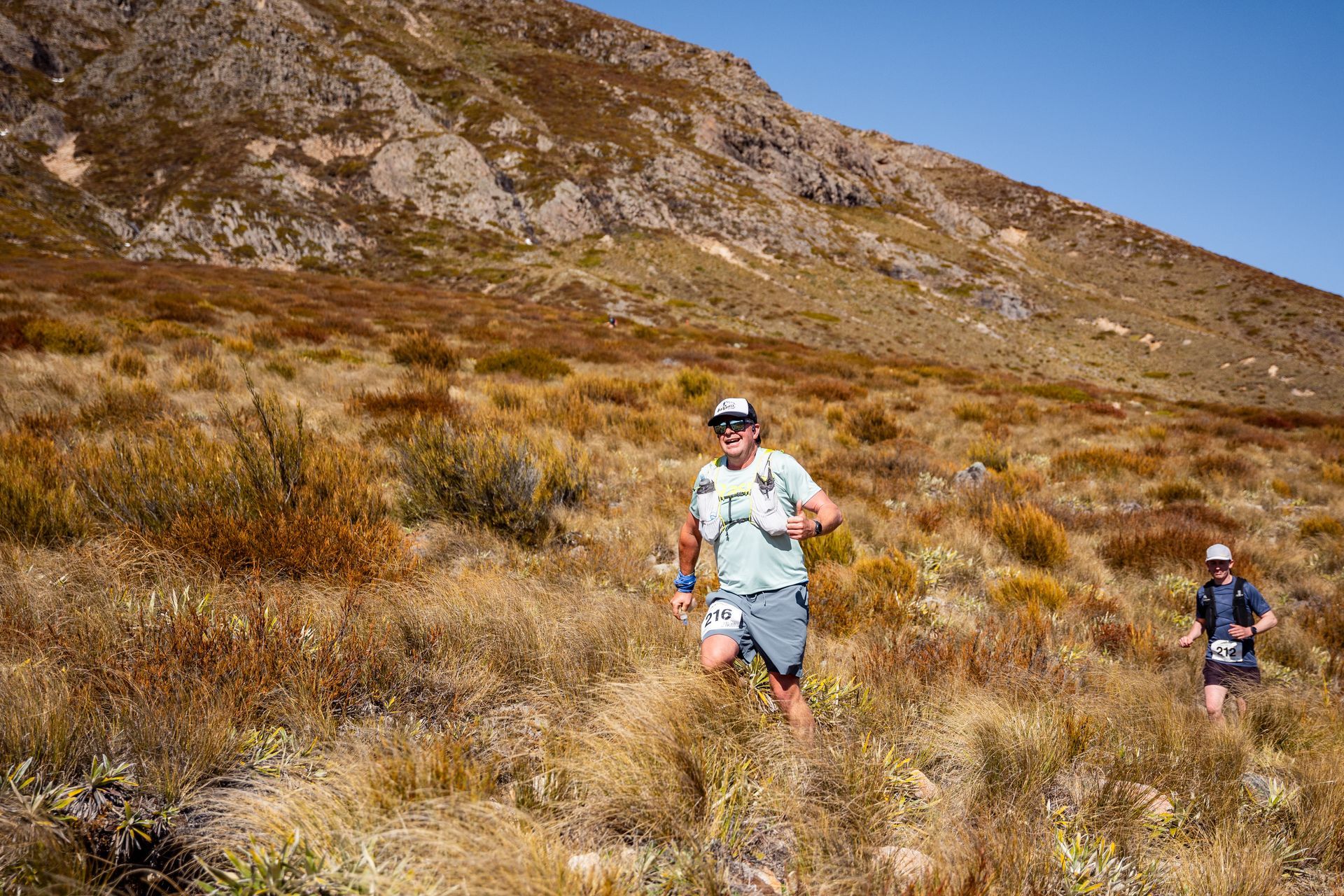 Two people are running on a trail in the mountains.