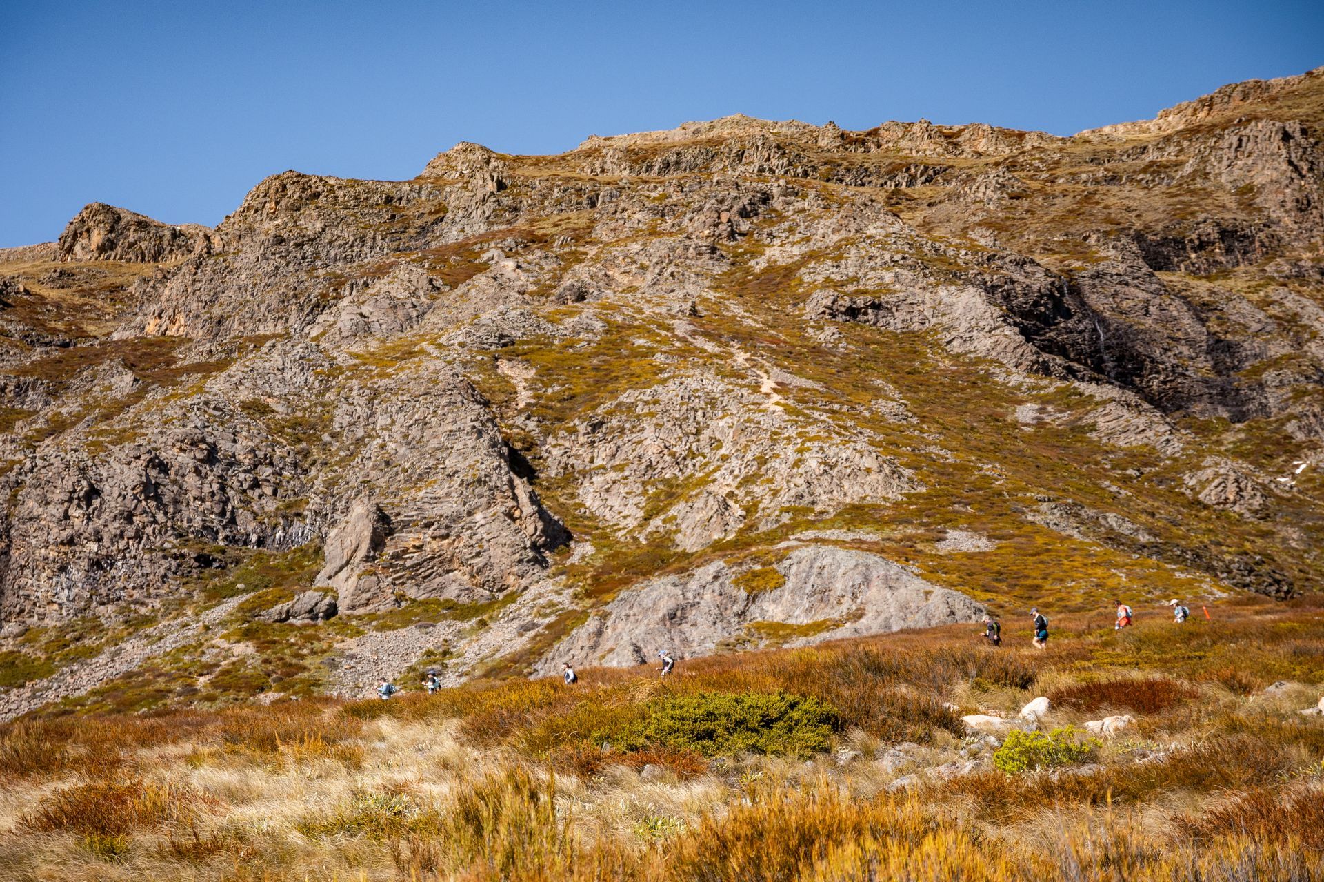 A mountain covered in grass and rocks with a blue sky in the background.