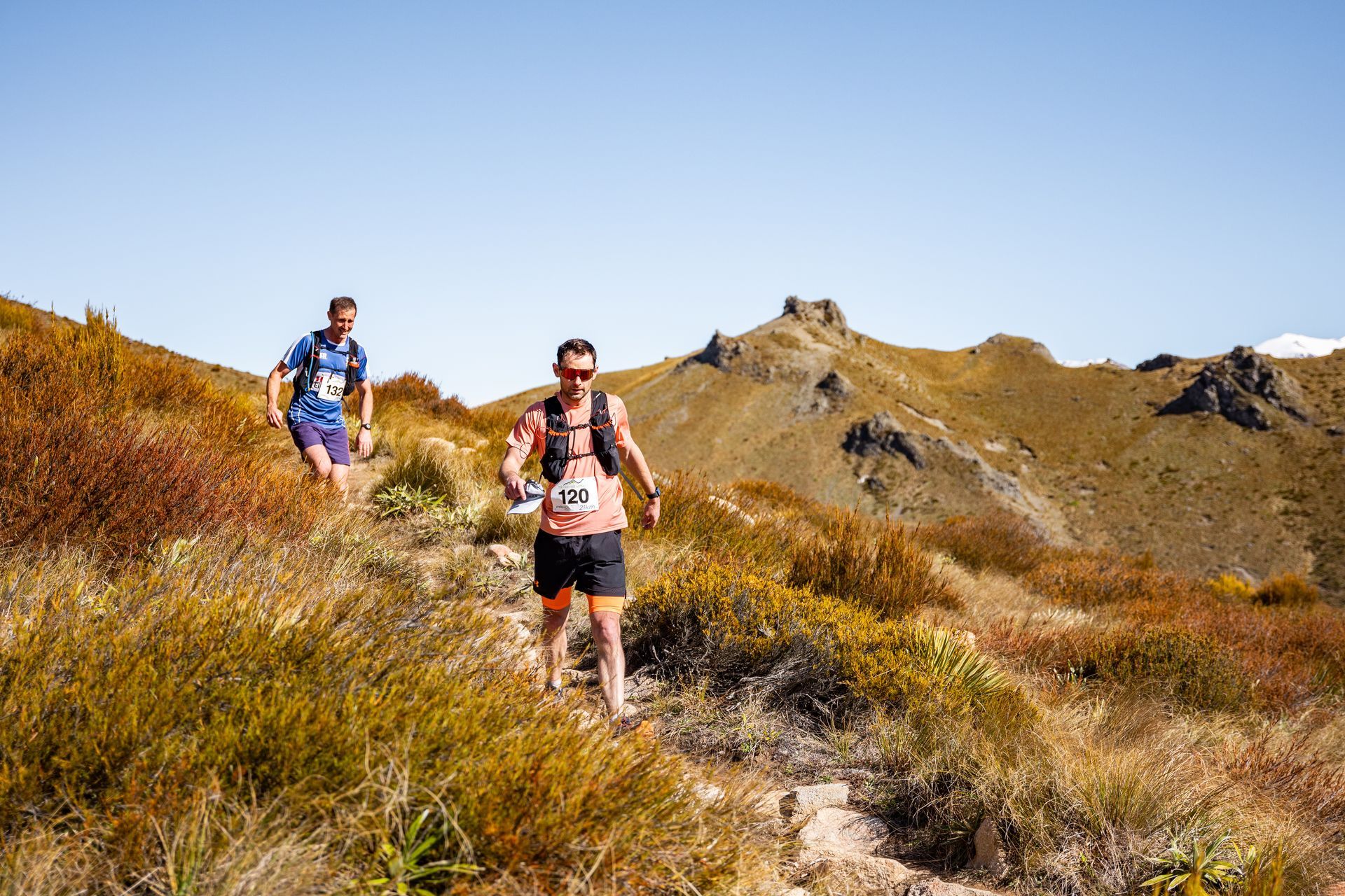 Two men are running on a trail in the mountains.