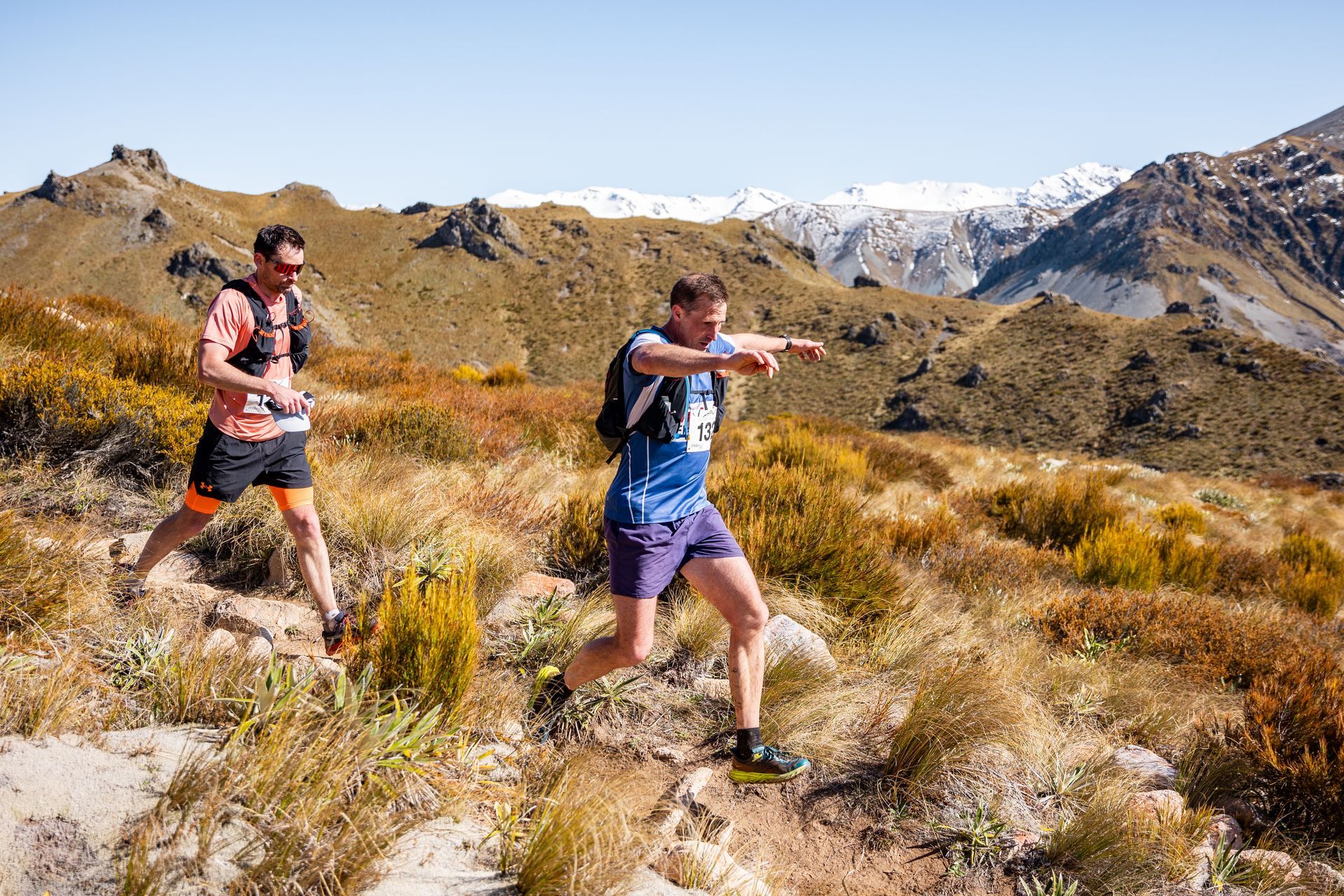 Two men are running on a trail in the mountains.