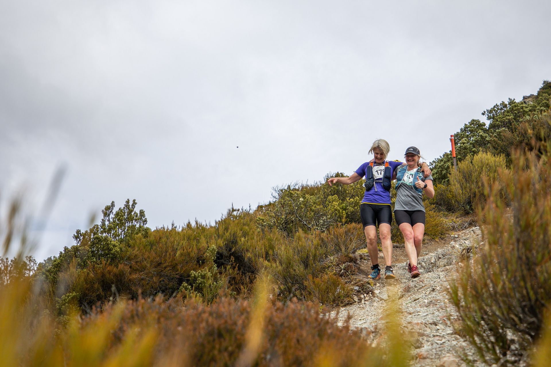 Two people are running up a hill on a trail.