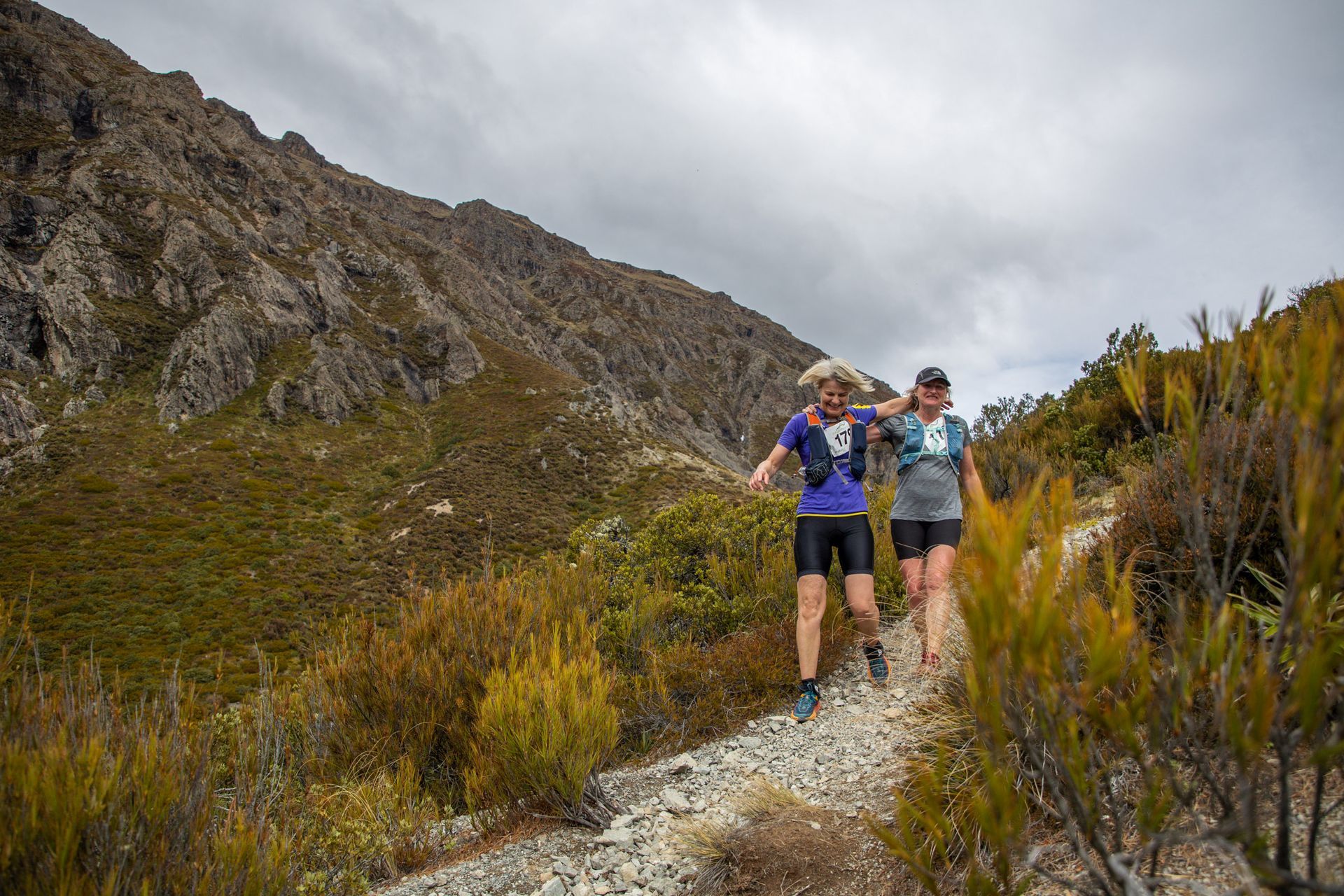 Two people are walking on a trail in the mountains.