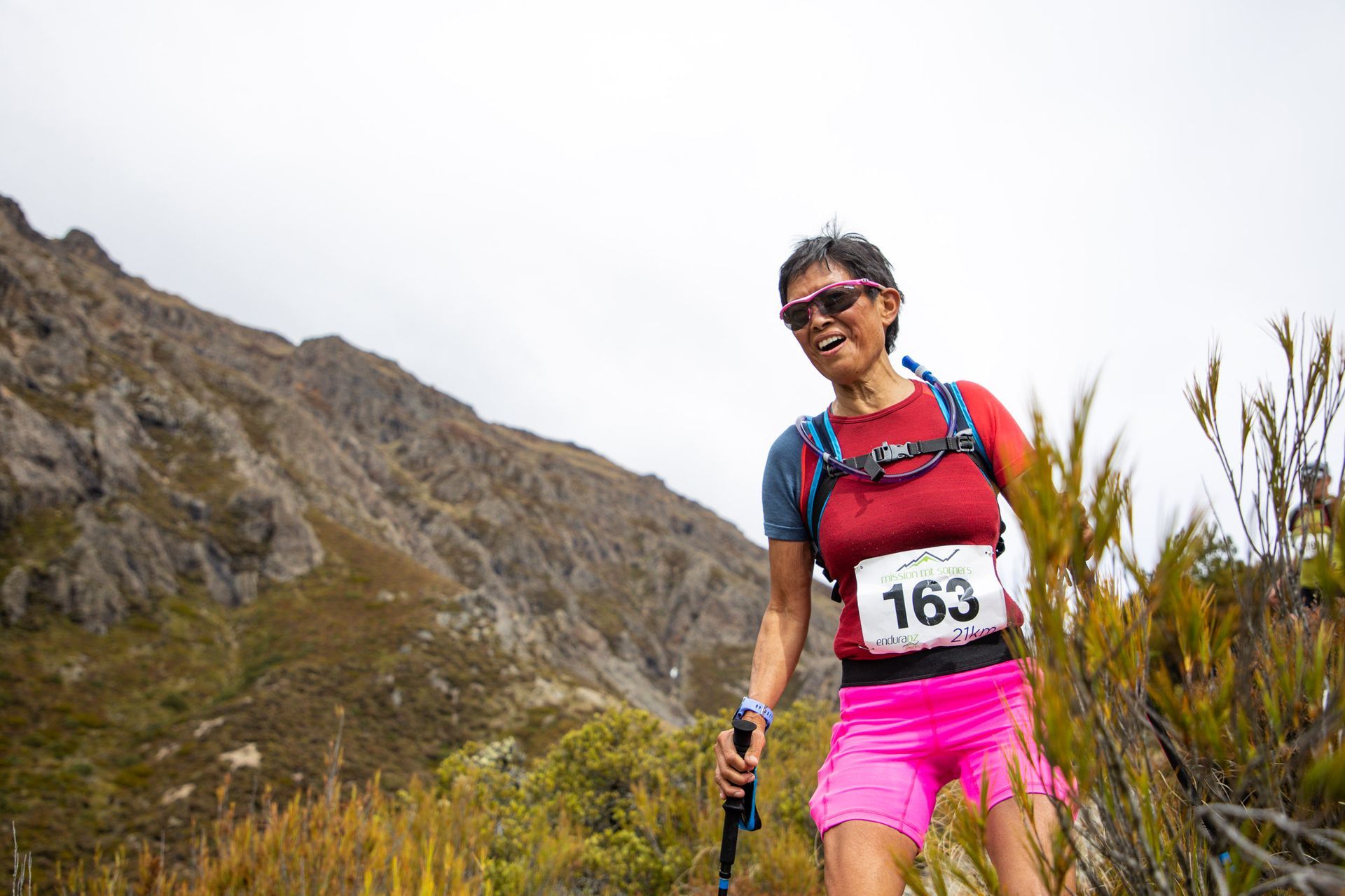 A woman is walking on a trail in the mountains with hiking poles.