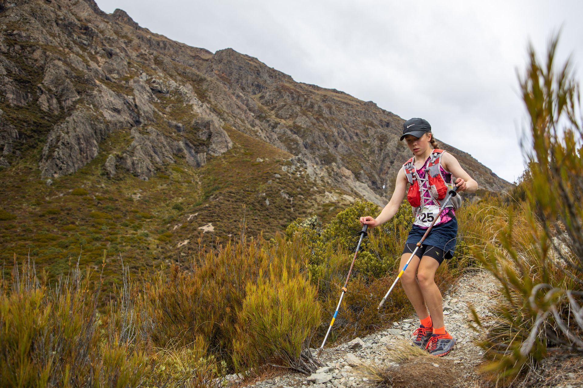 A woman is walking on a trail in the mountains with hiking poles.