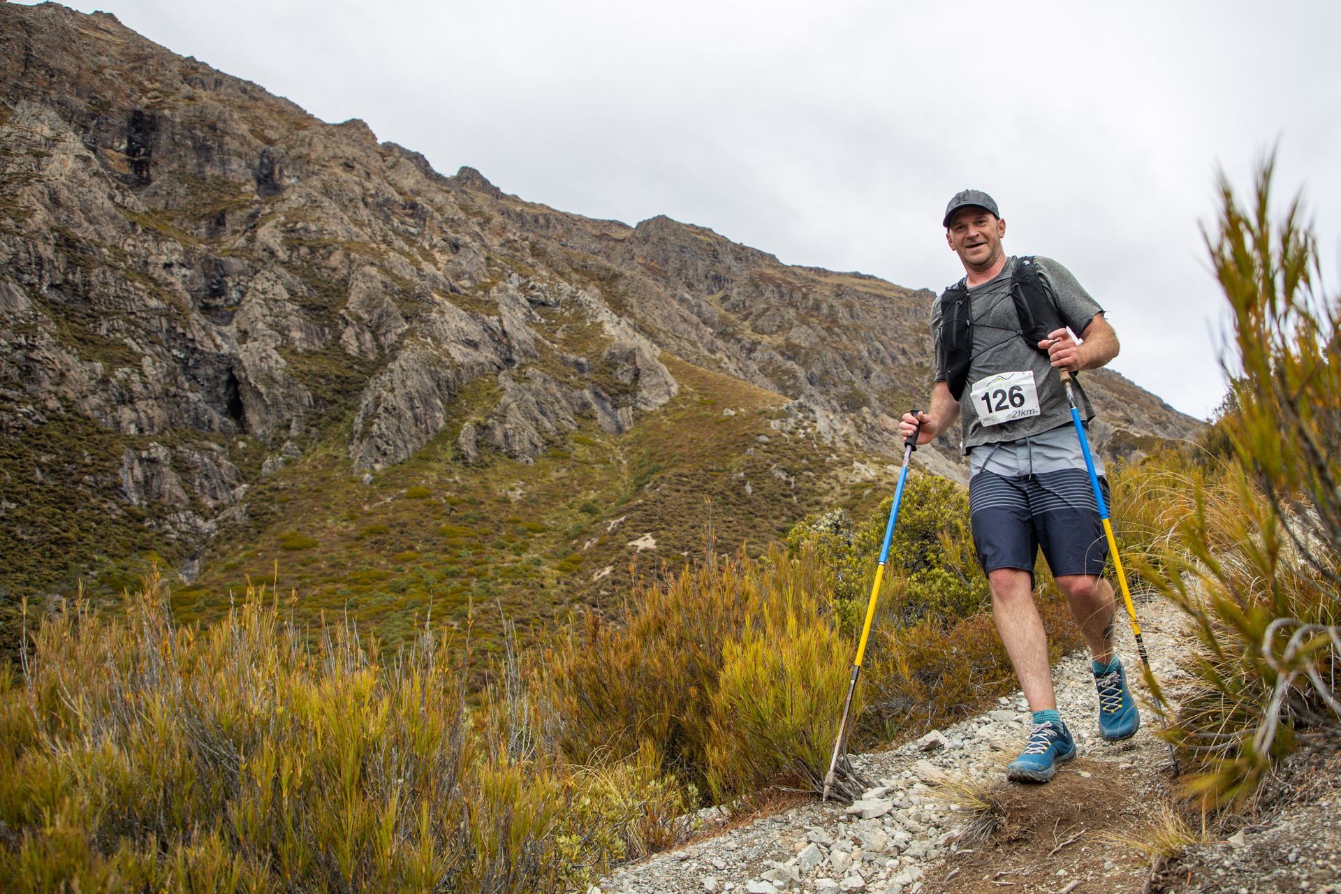 A man is walking on a trail in the mountains with hiking poles.