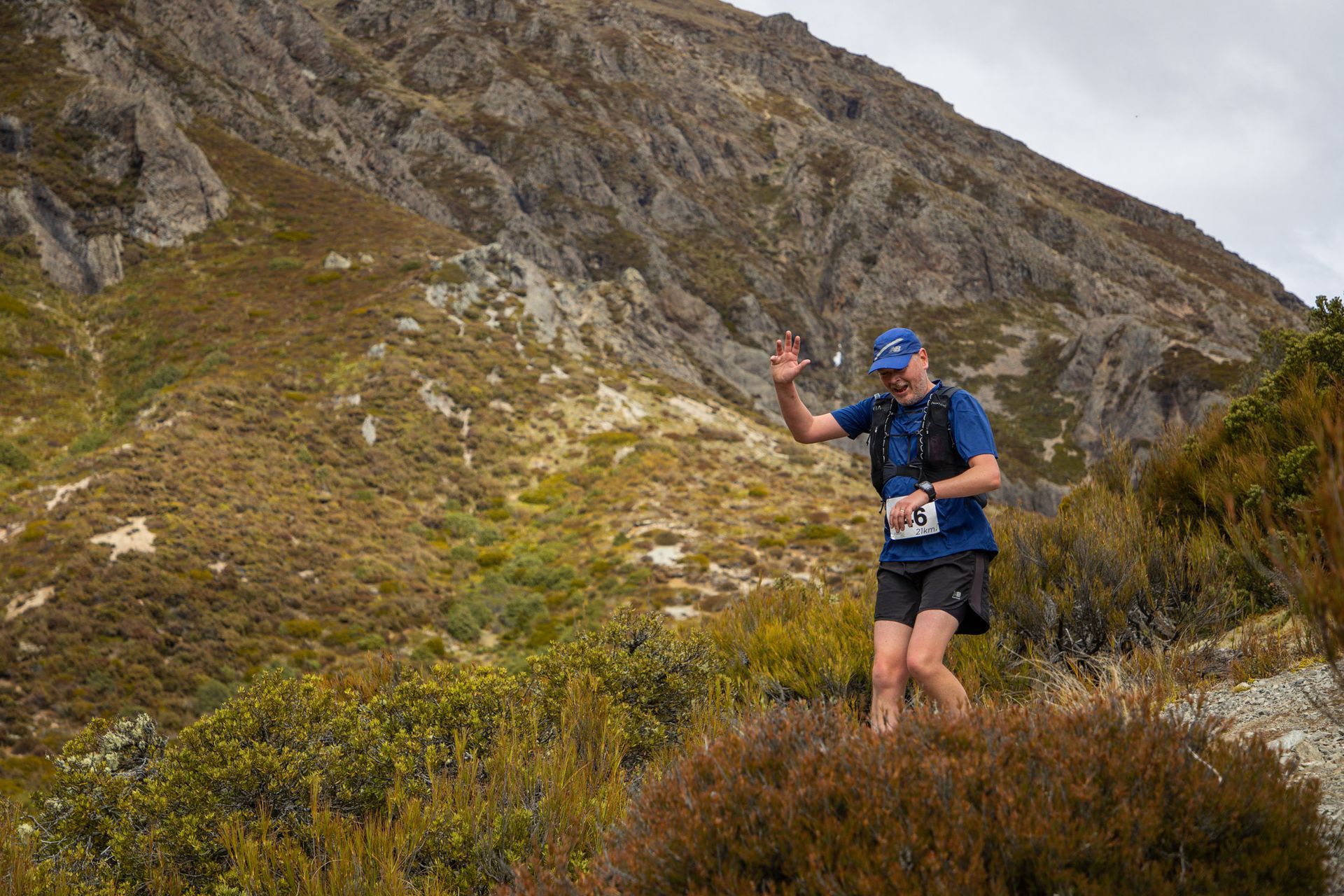 A man in a blue shirt and black shorts is standing on top of a hill.