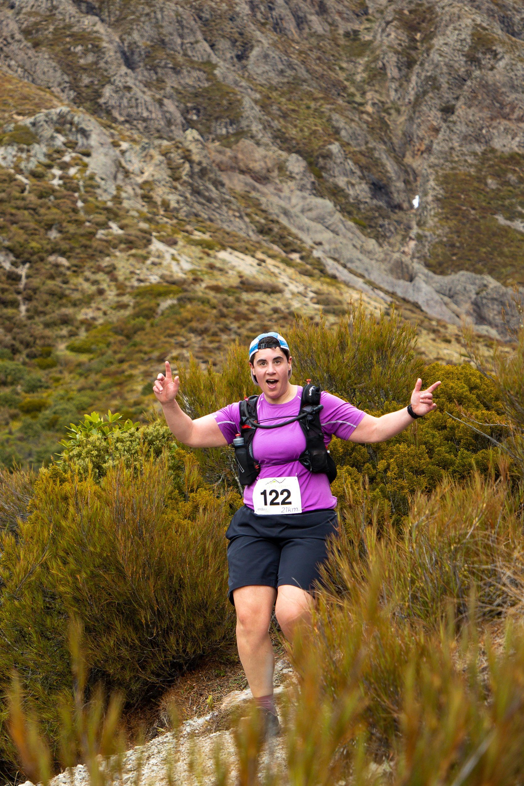 A woman is running on a trail in the mountains with her arms outstretched.