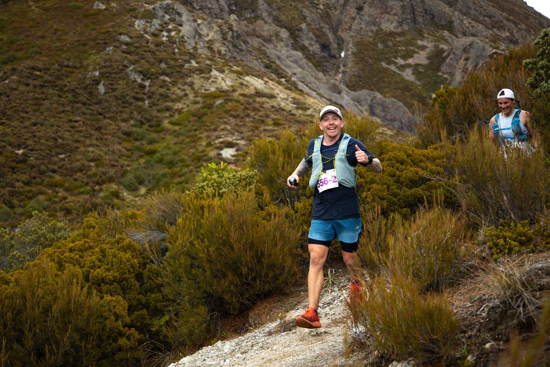 Two people are running on a trail in the mountains.
