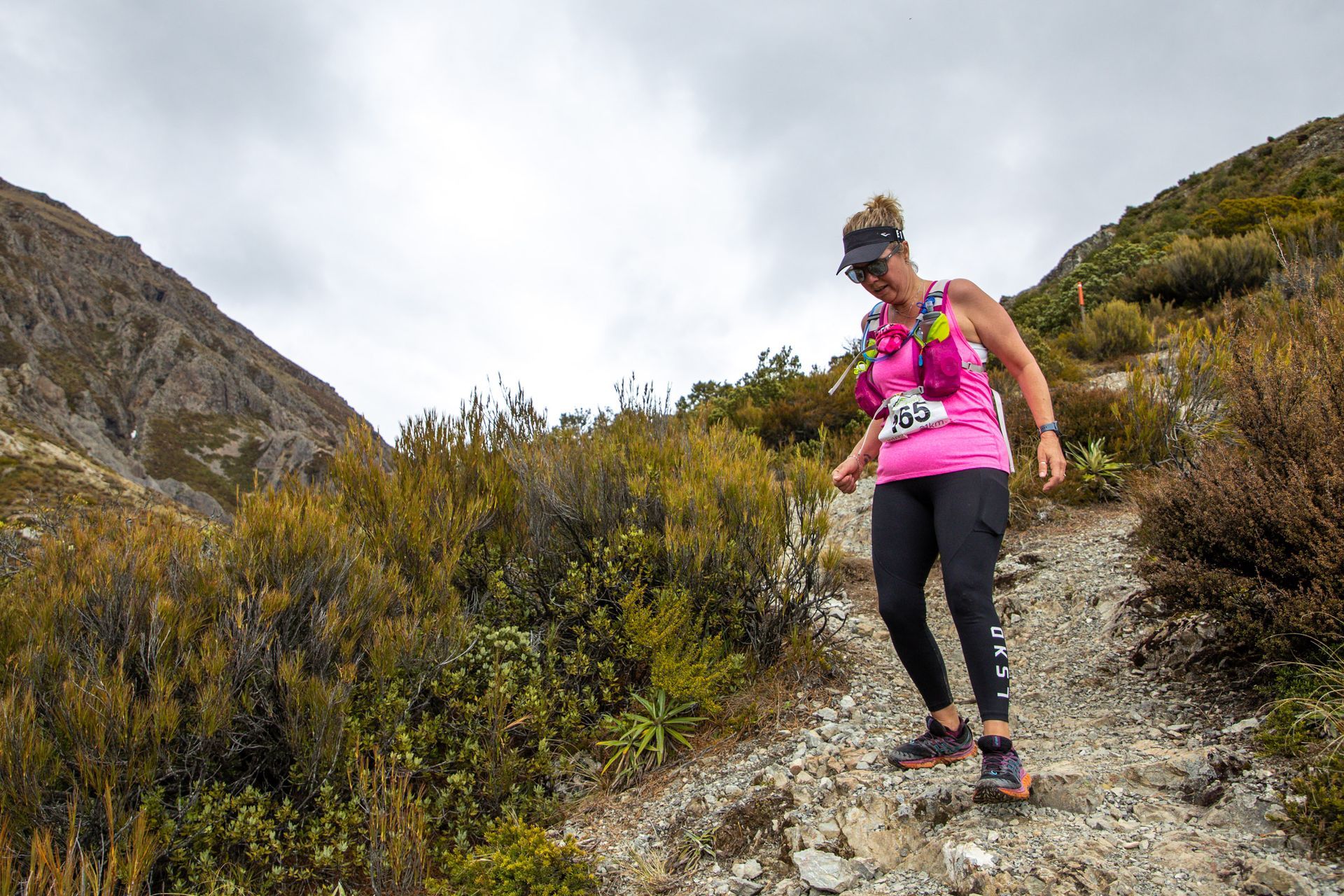 A woman in a pink tank top is walking down a dirt path.