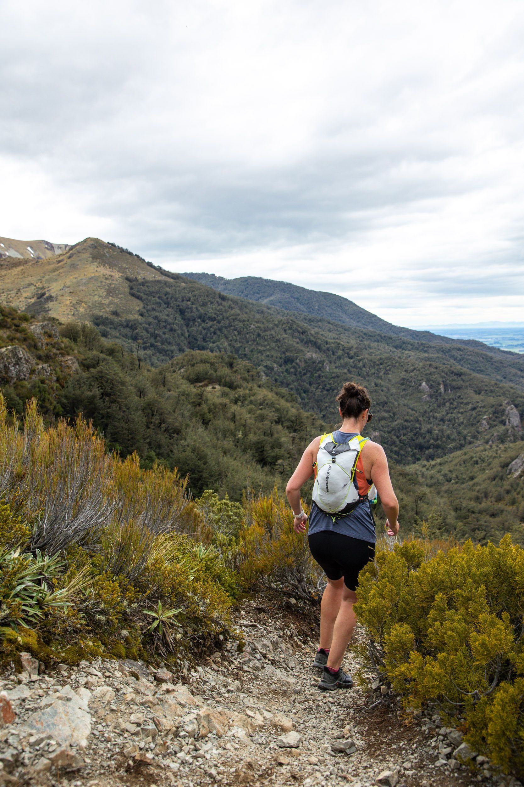 A woman is running on a trail in the mountains.