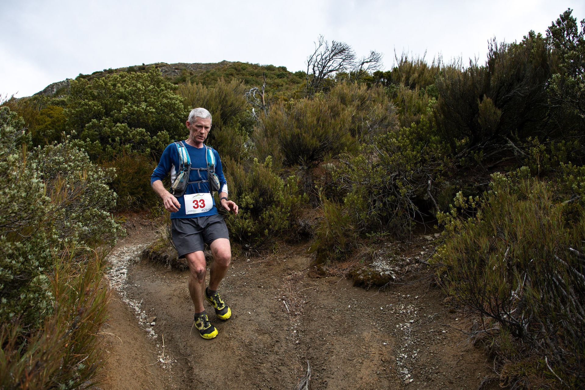 A man is running down a dirt path in the woods.