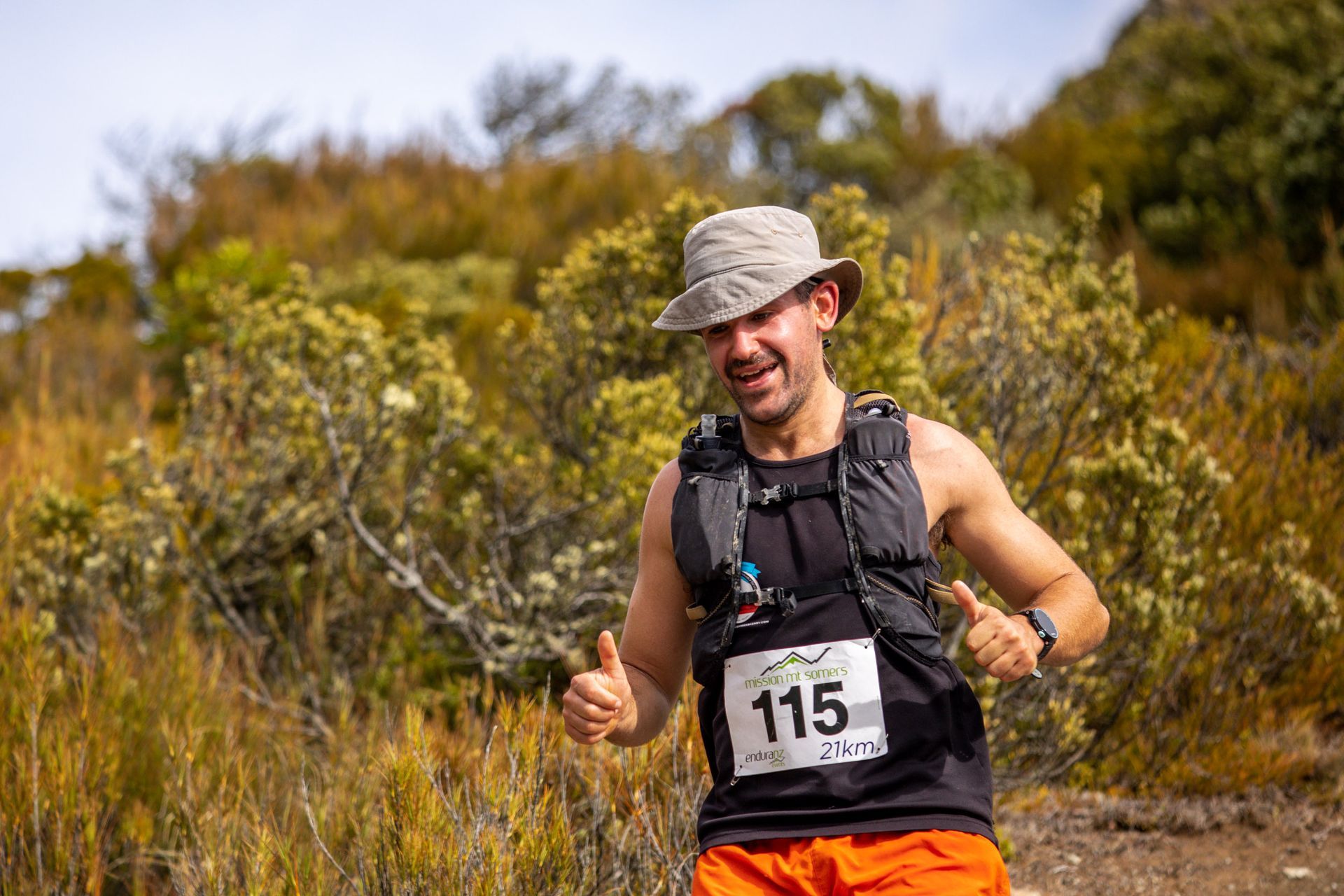 A man is running in a field wearing a hat and giving a thumbs up.