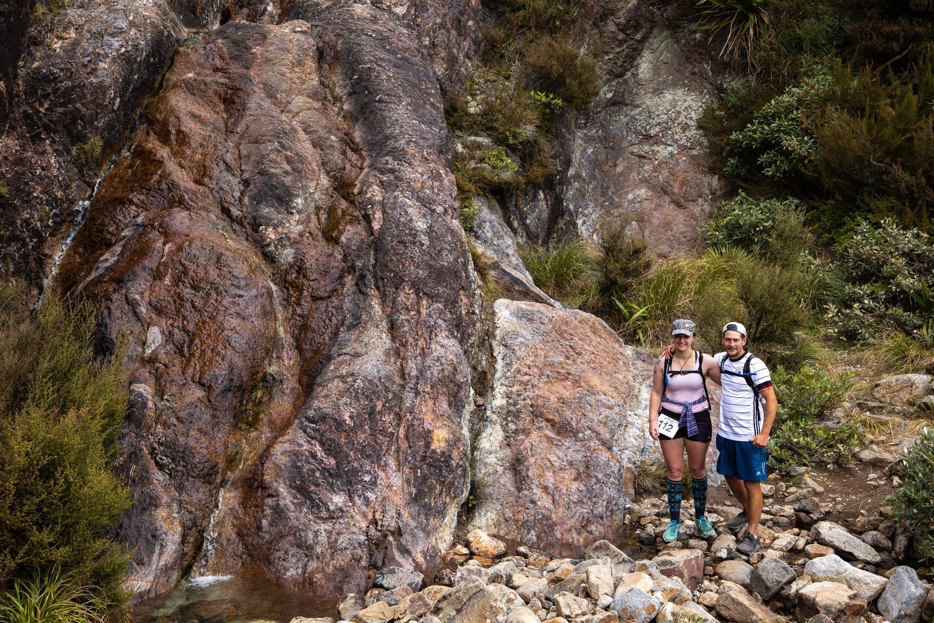 A man and a woman are standing next to each other in front of a large rock.
