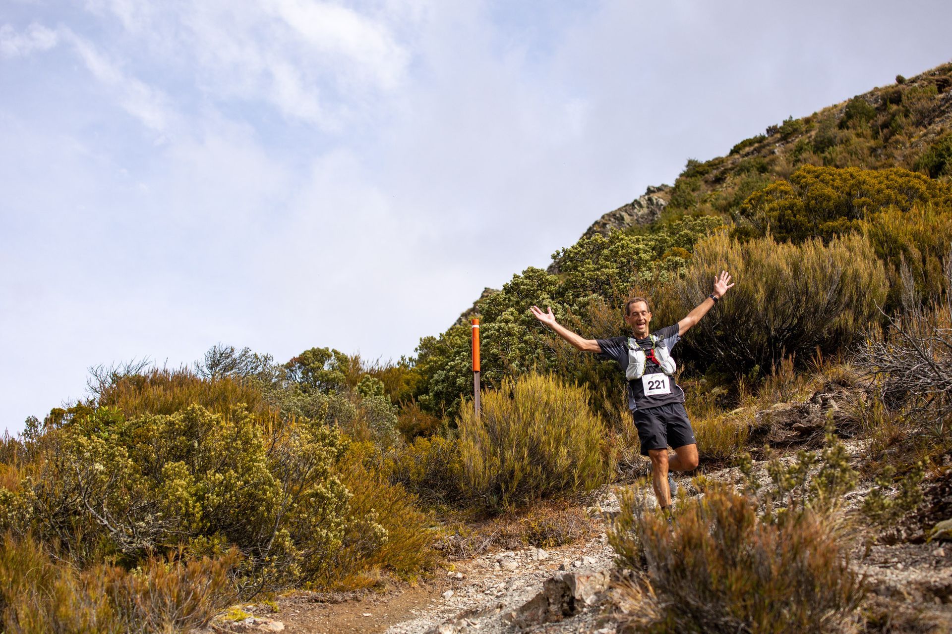 A man is standing on top of a hill with his arms outstretched.