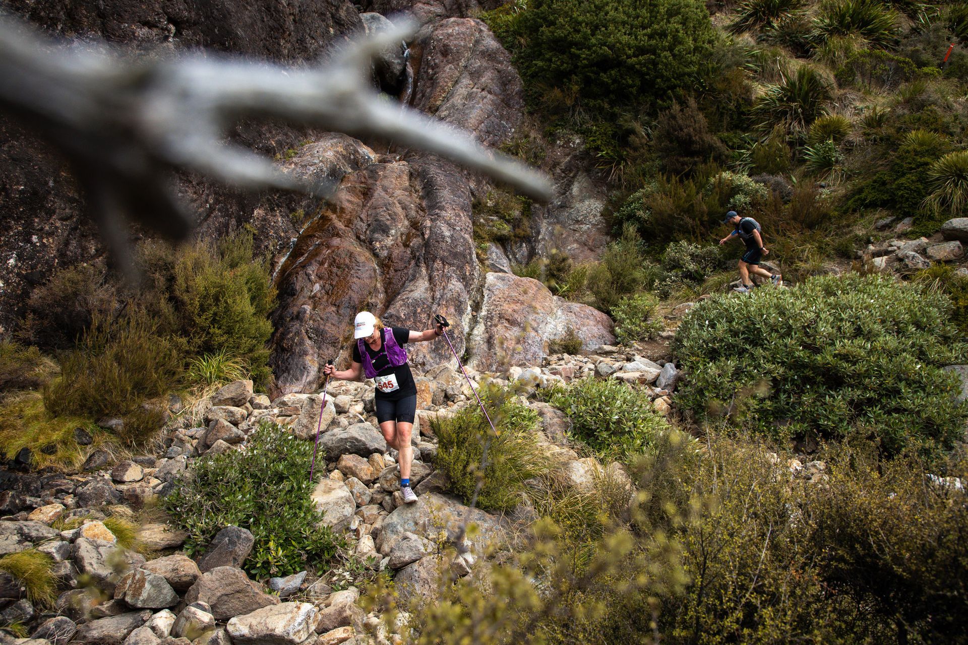 A woman is running down a rocky trail in the woods.