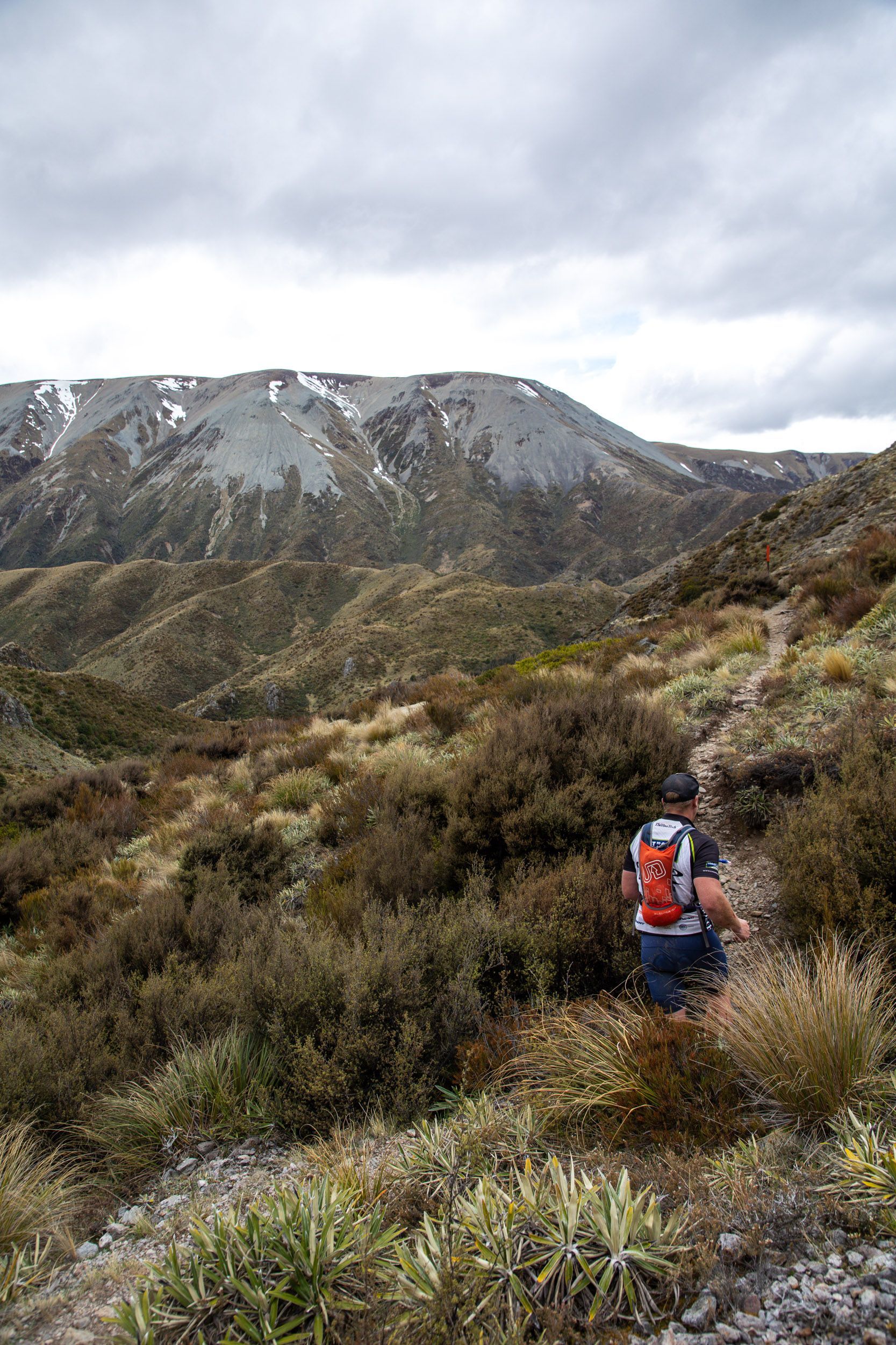A man with a backpack is walking down a trail in the mountains.
