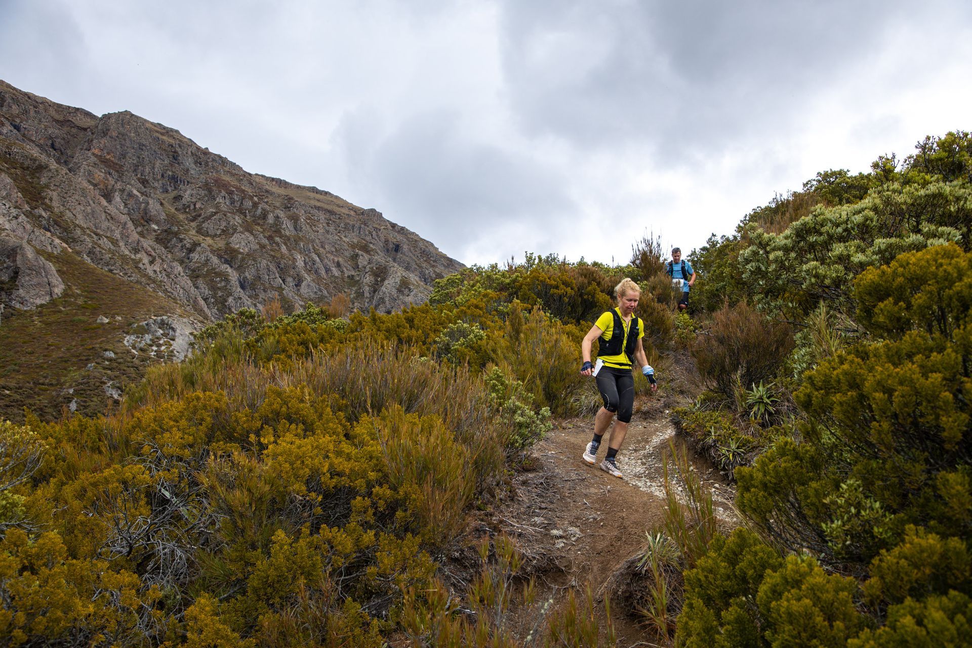 A man is running down a trail in the mountains.