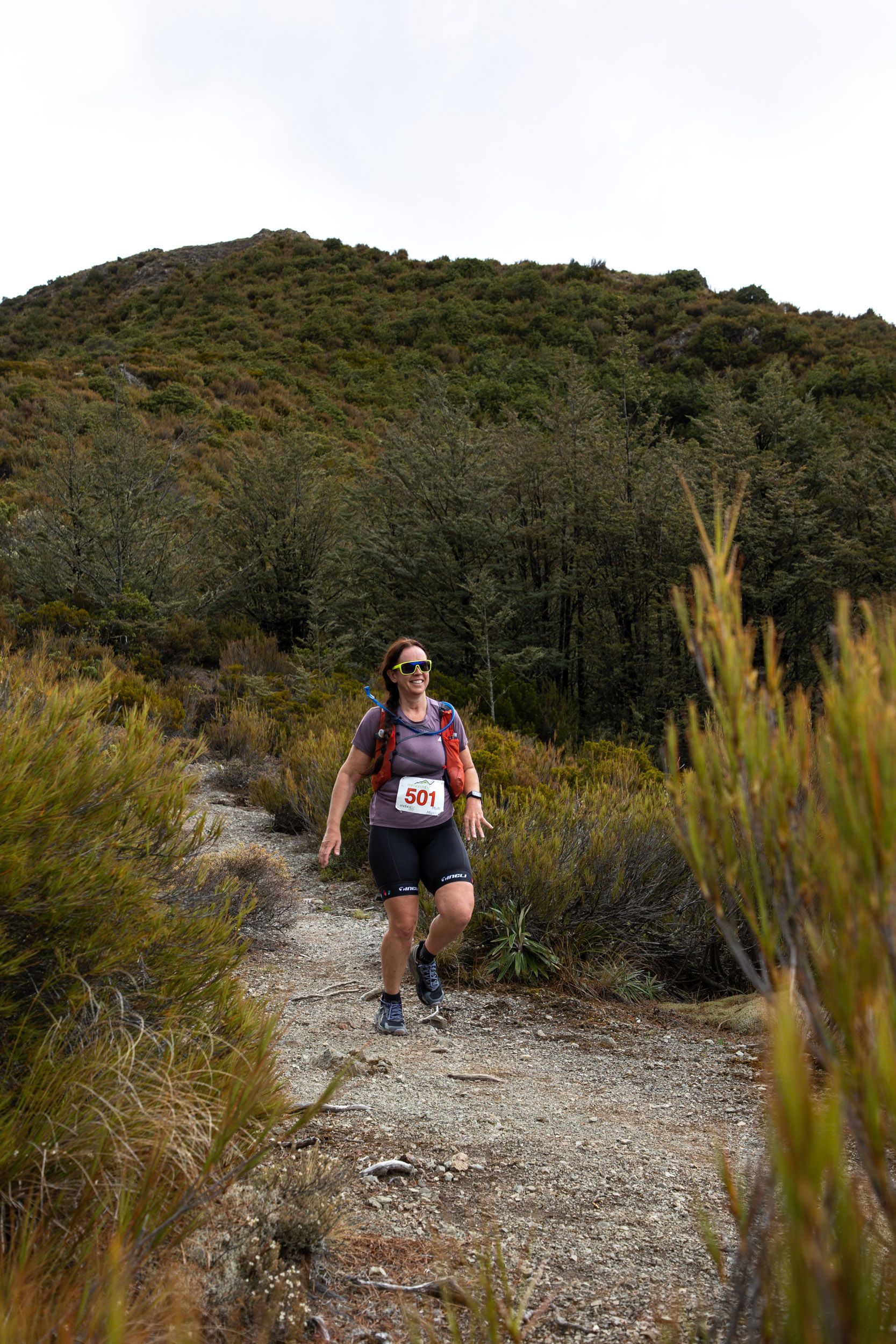 A woman is running down a dirt path in the woods.