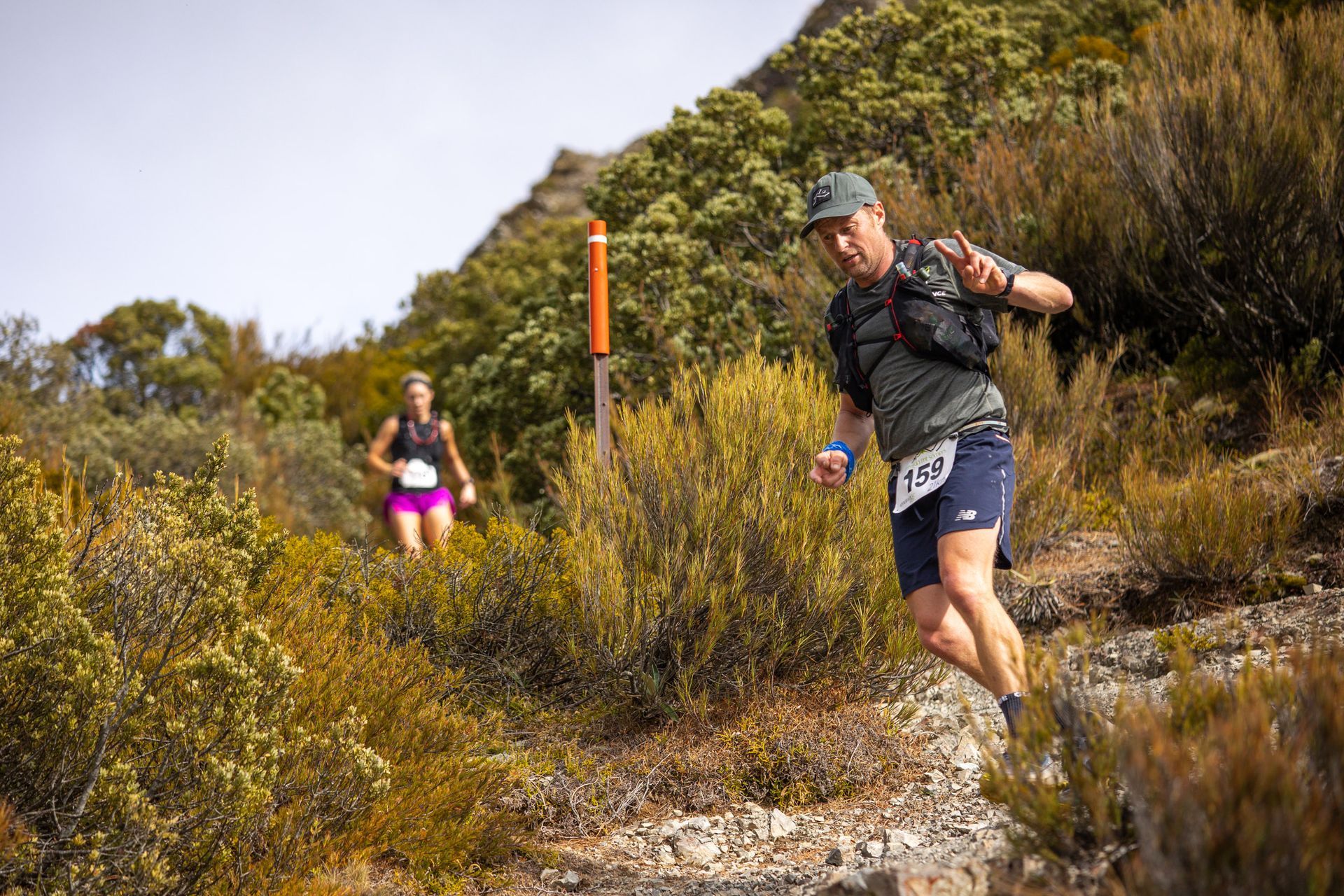 A man and a woman are running on a trail in the woods.