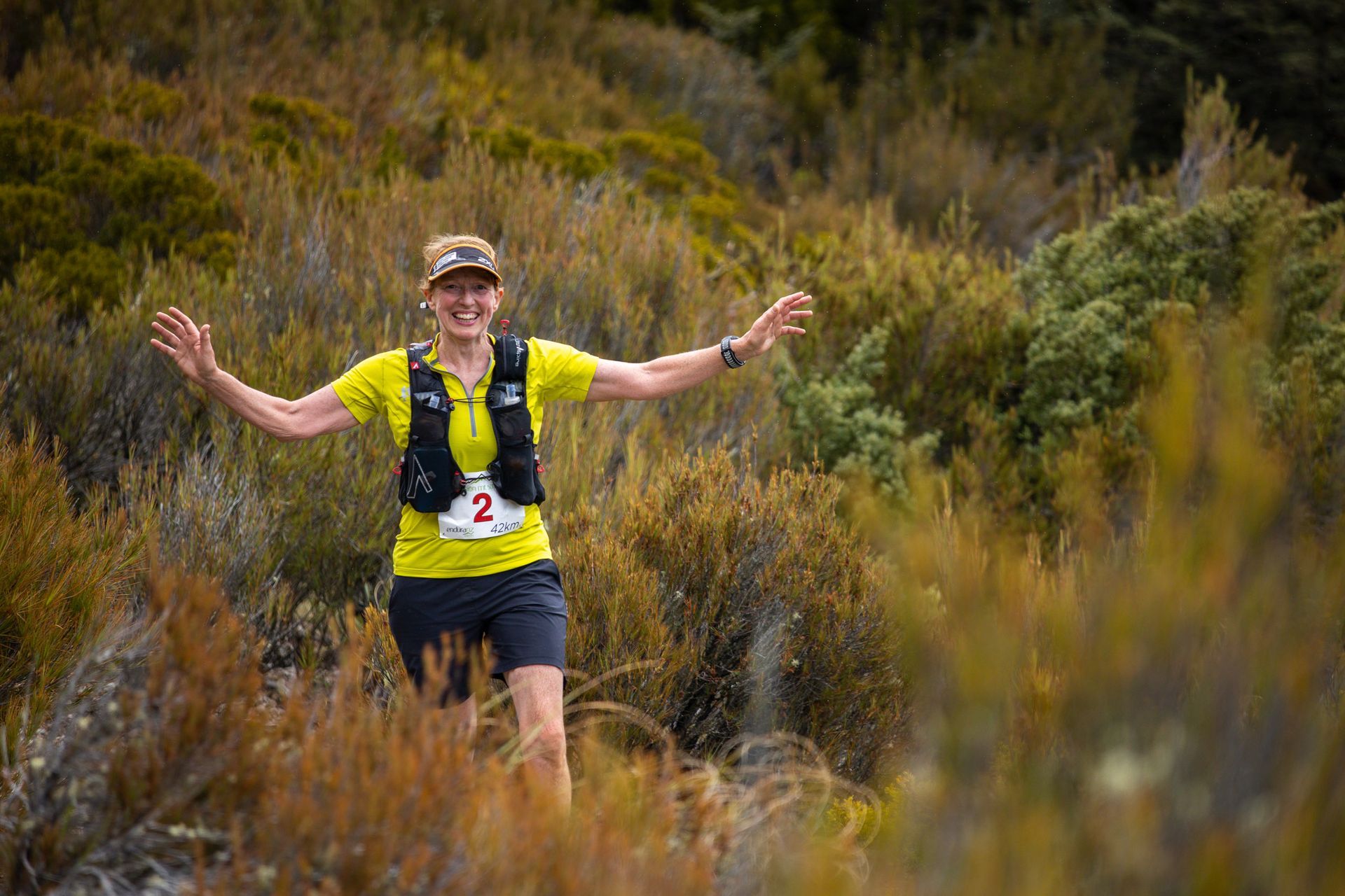 A woman is running through a field with her arms outstretched.