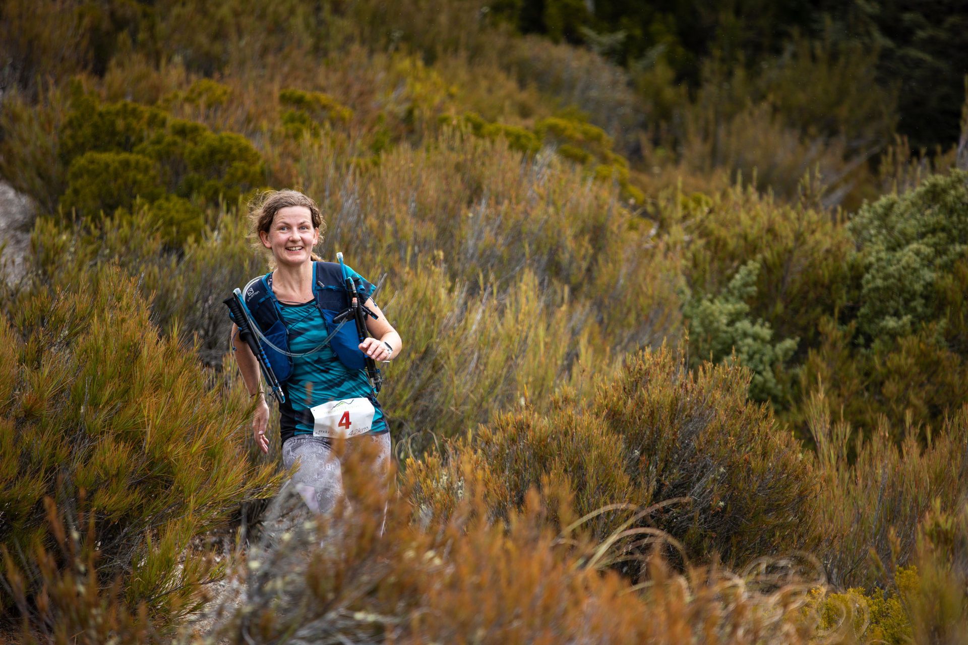 A woman is running through a field of tall grass.
