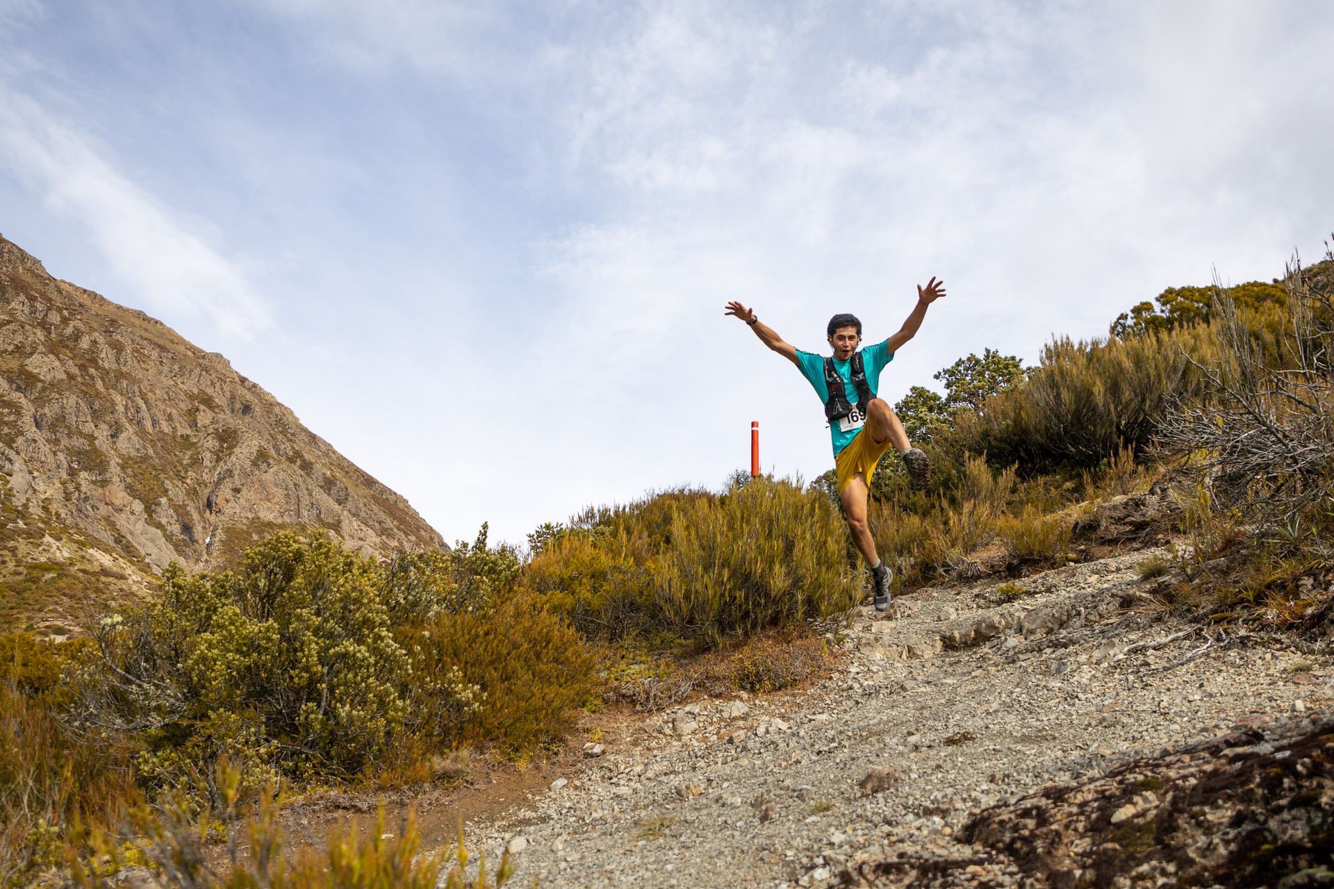 A man is jumping in the air while running down a dirt trail.