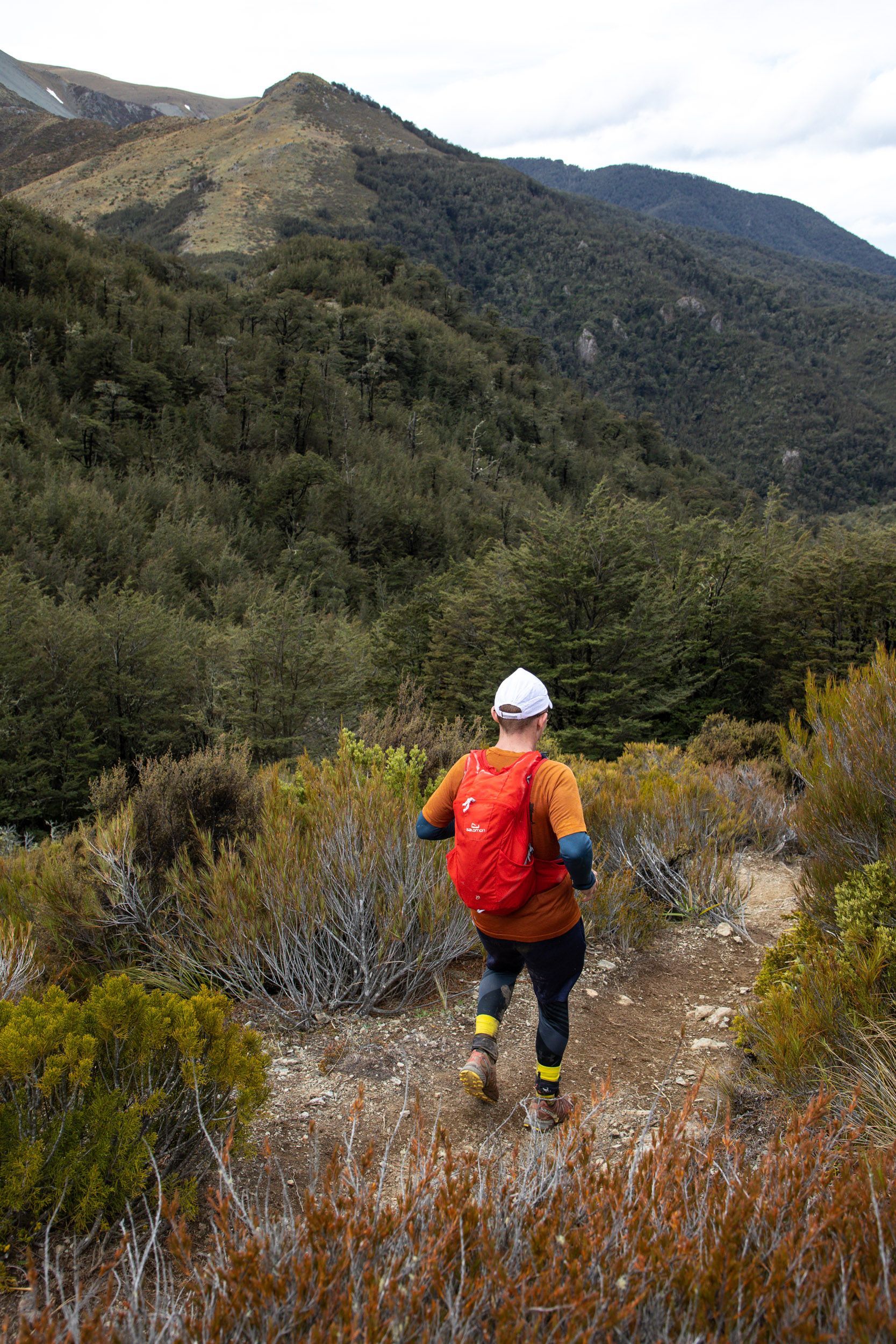 A person with a backpack is running on a trail in the woods.