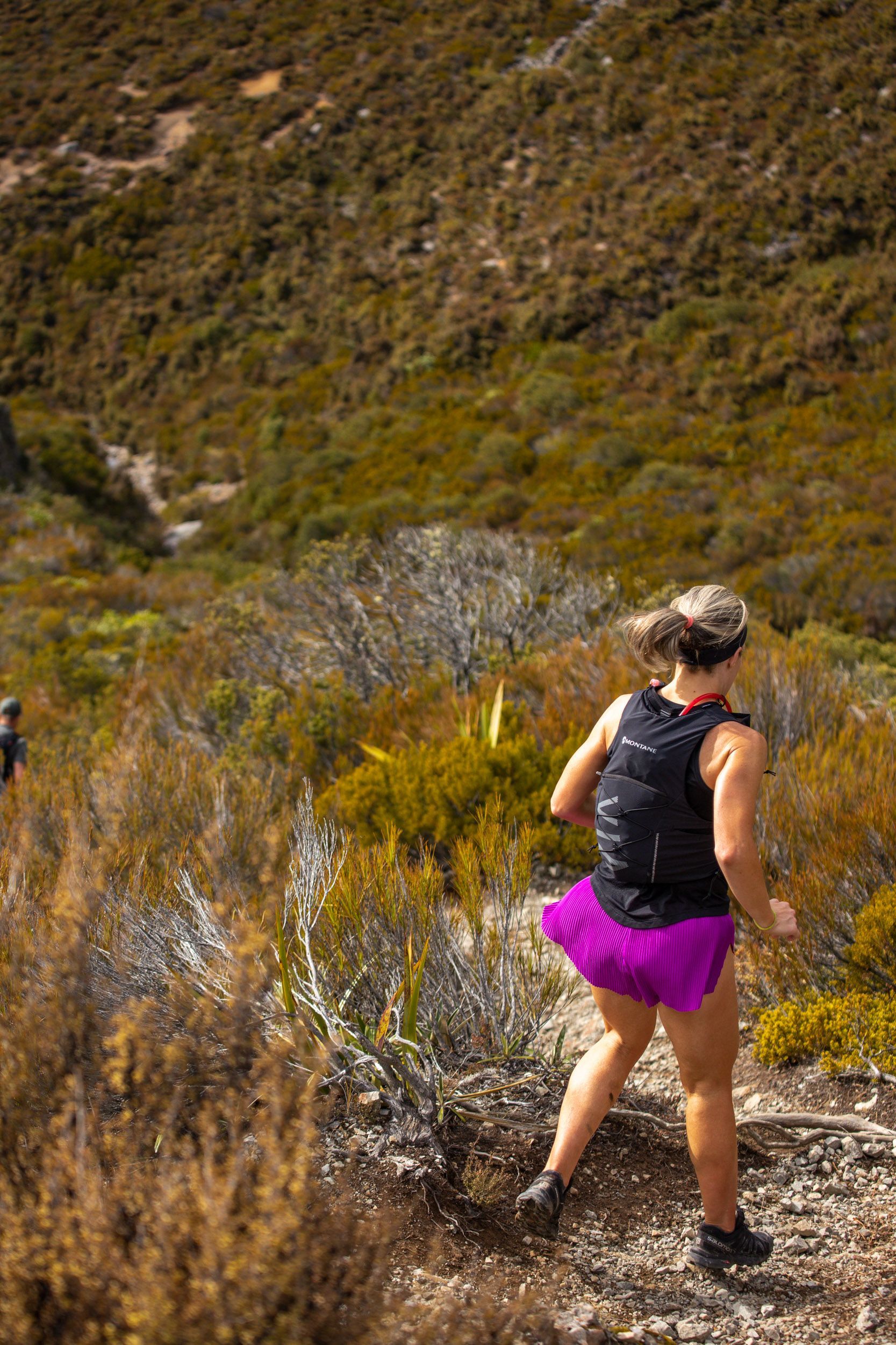 A woman is running up a hill on a trail.