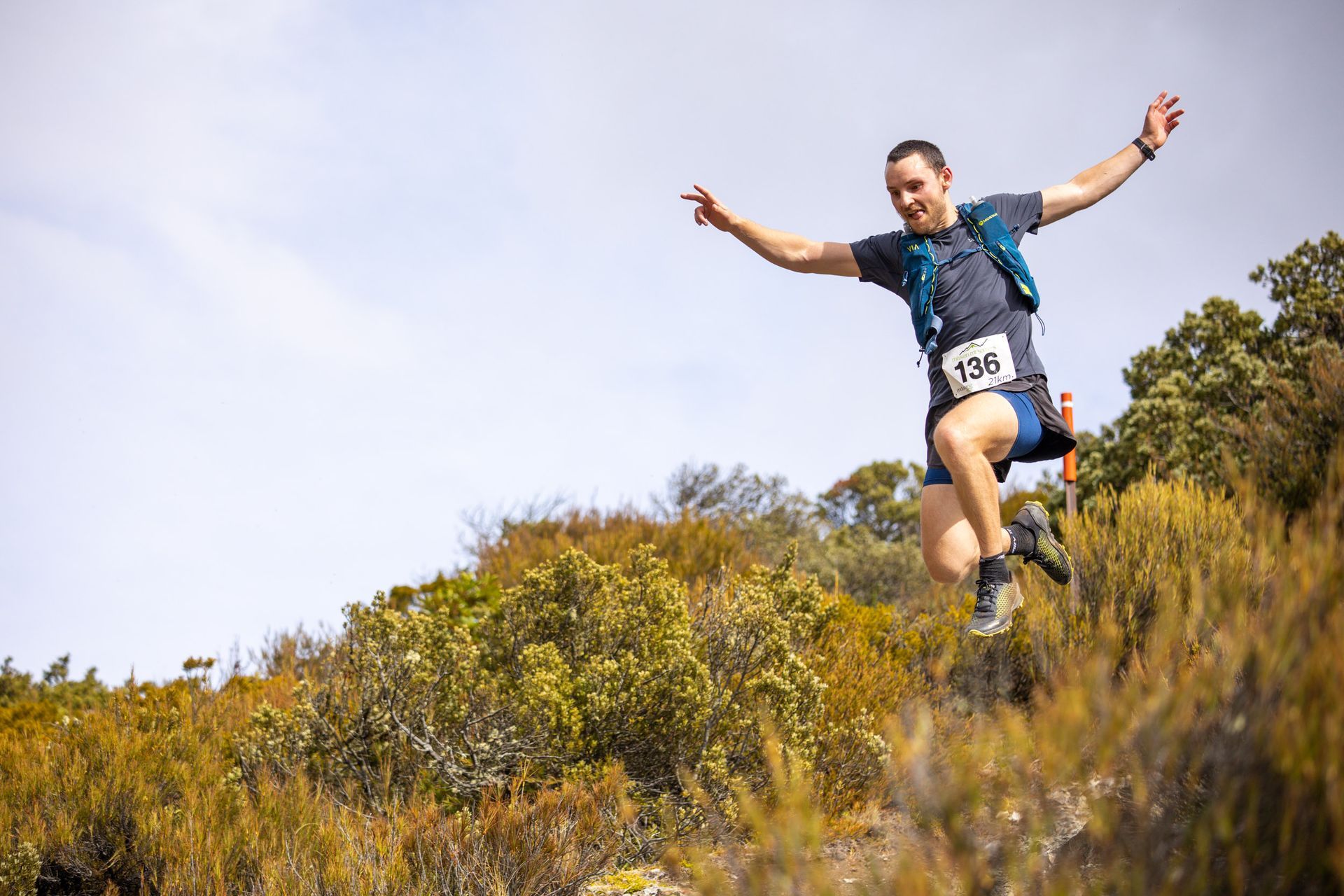 A man is jumping in the air while running on a trail.