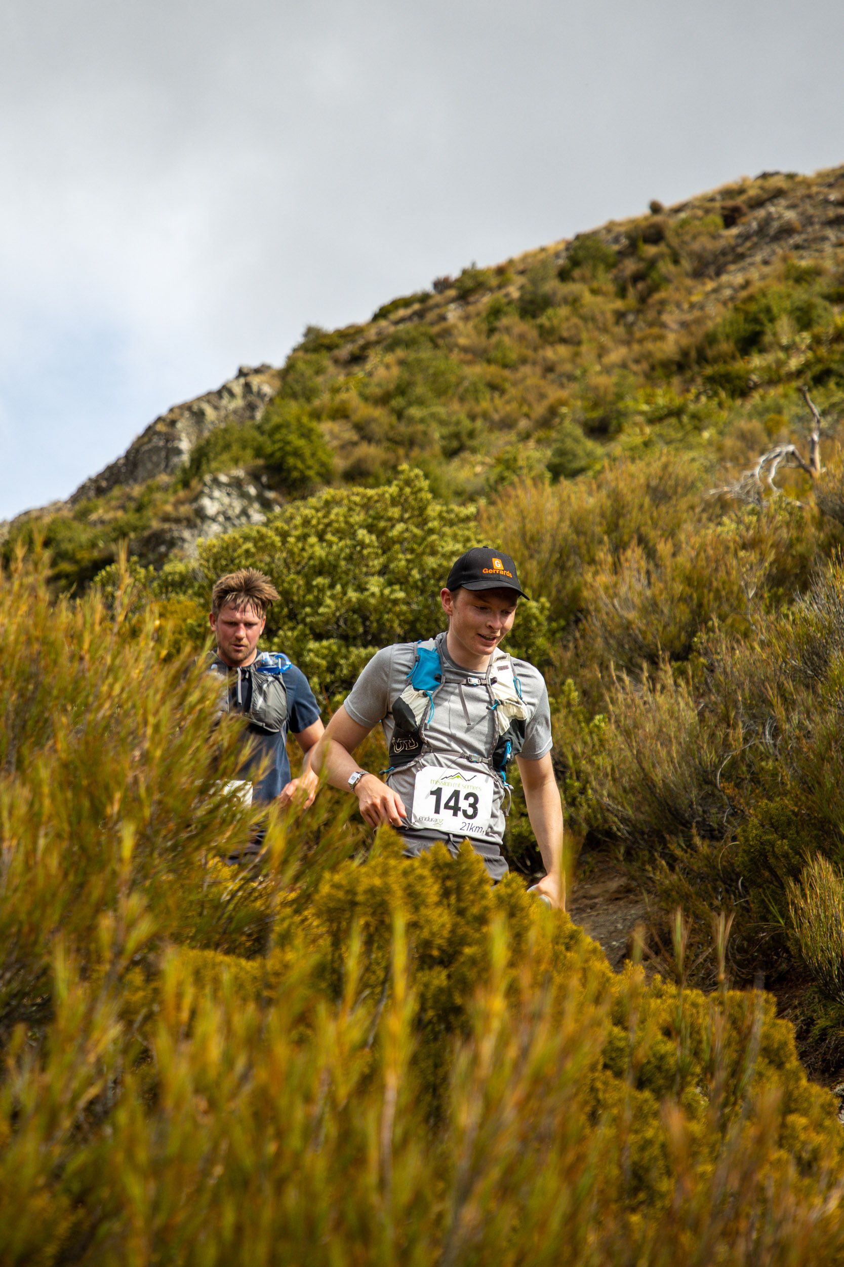Two men are running up a hill in the woods.