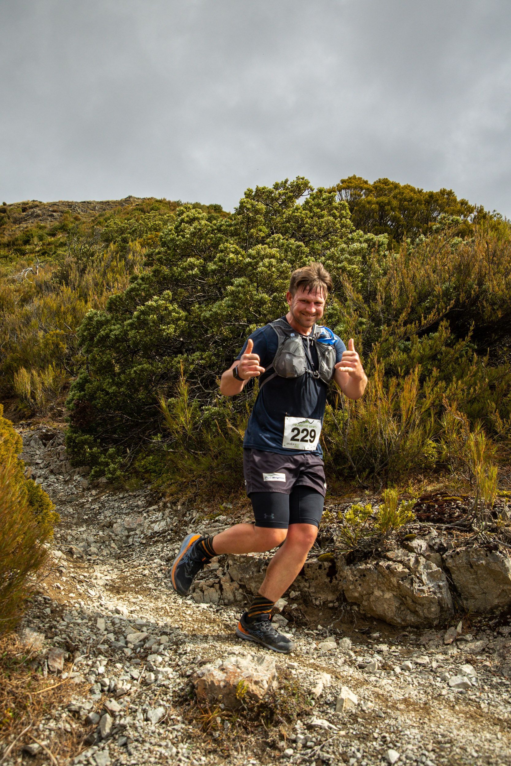 A man is running on a rocky trail and giving a thumbs up.