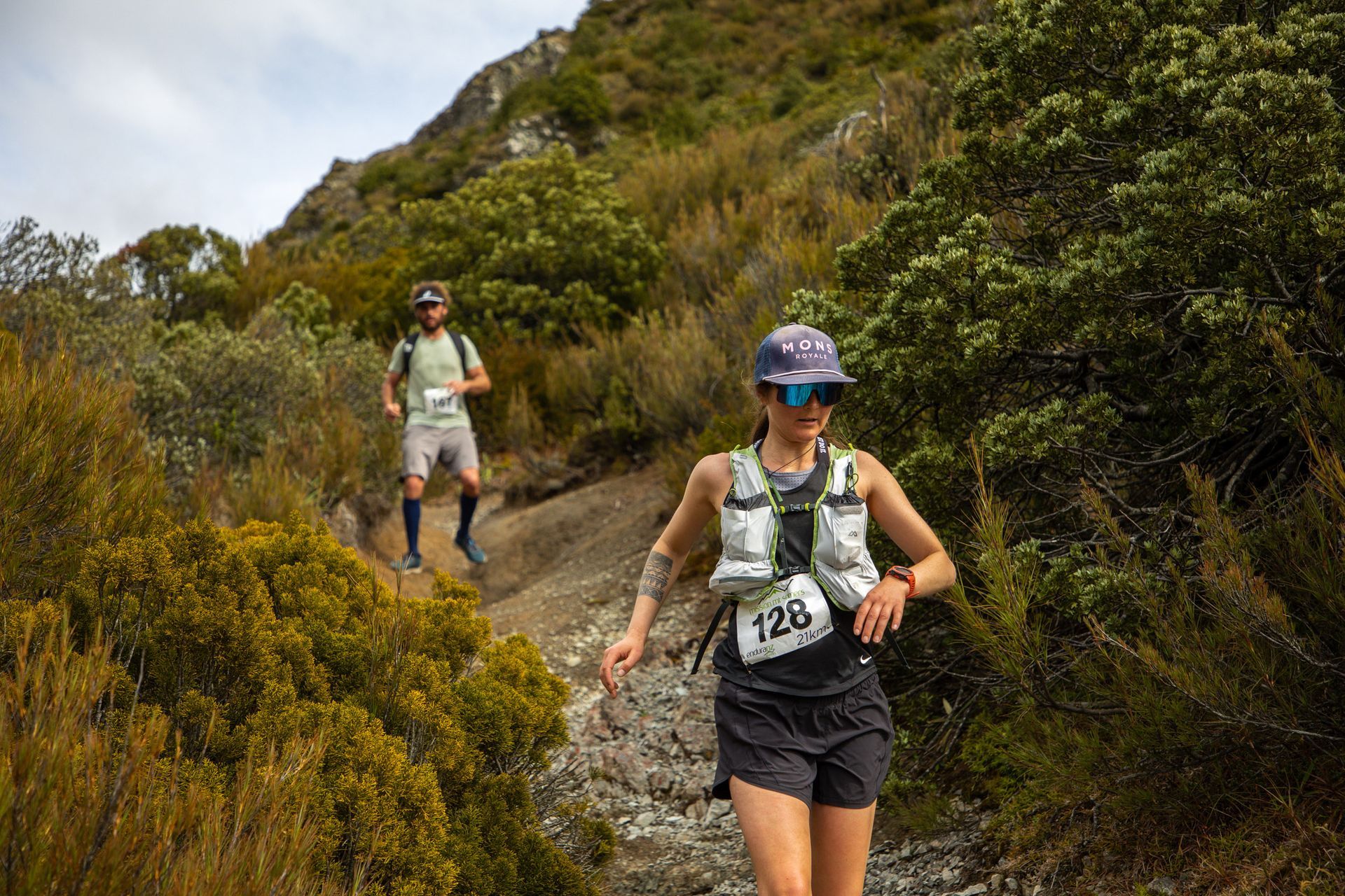 A man and a woman are running on a trail in the woods.