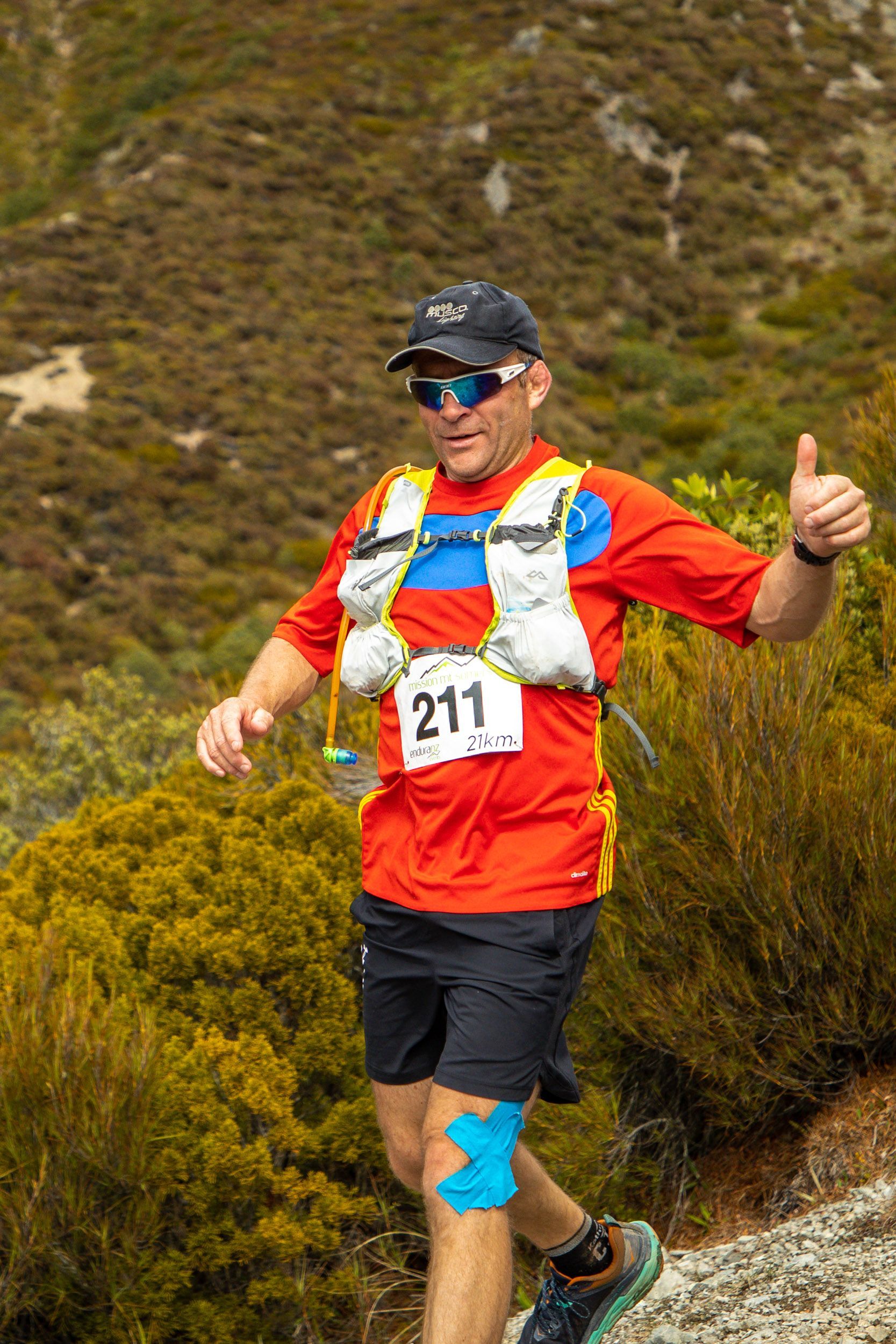 A man is running on a trail and giving a thumbs up.