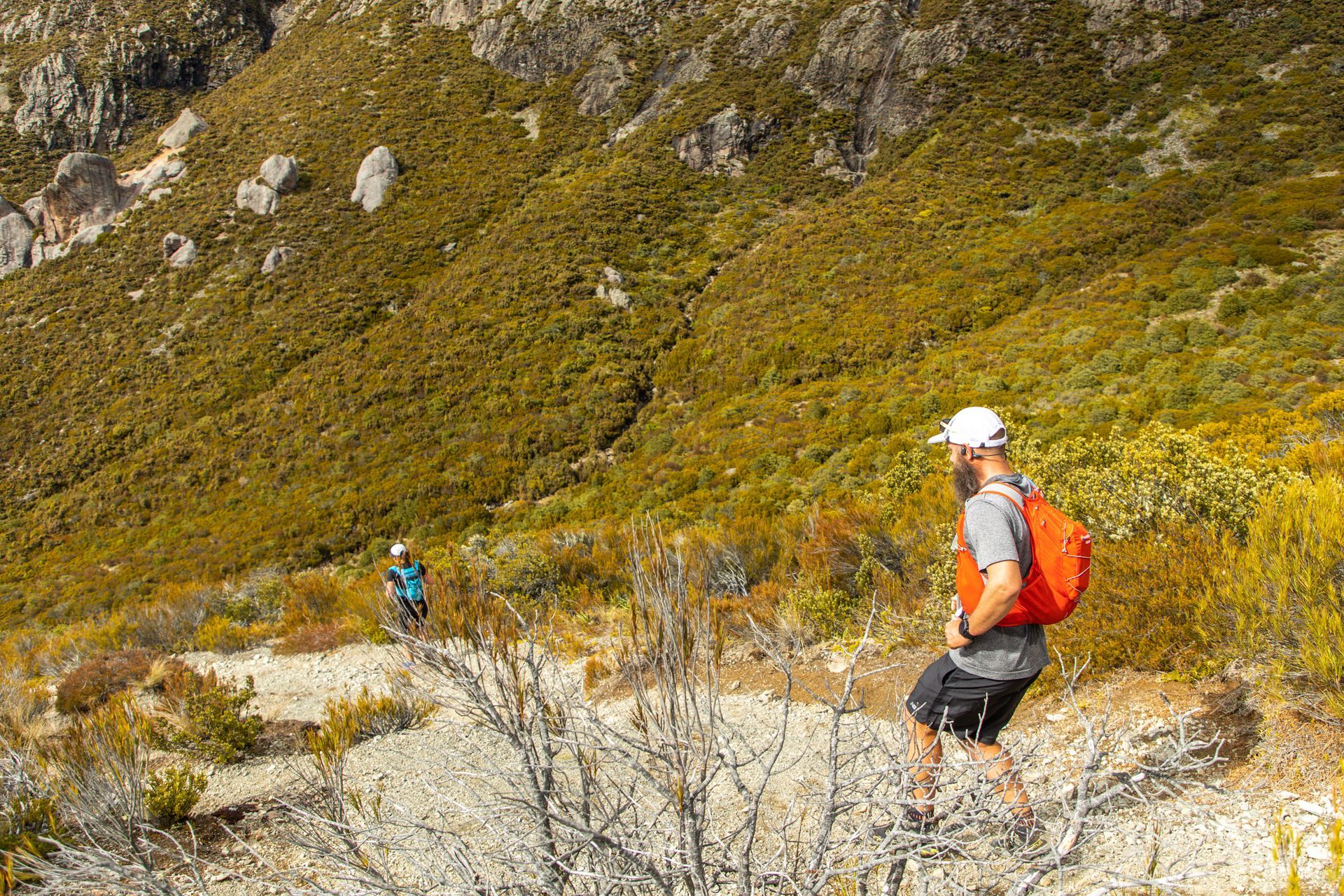 A man with an orange backpack is hiking up a hill.